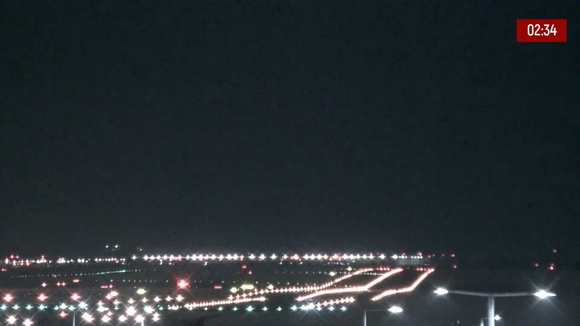 A nighttime long shot of an airport runway illuminated with lights under a clear, dark sky.