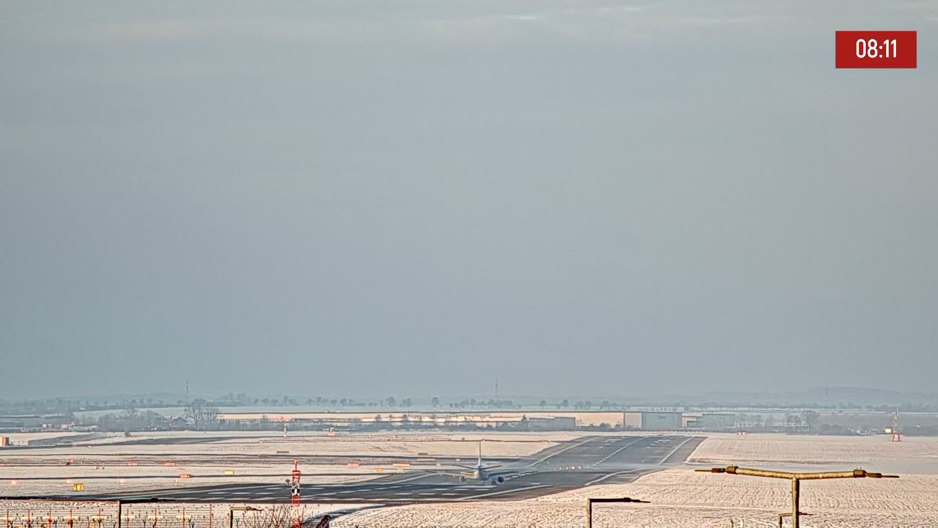 A plane is landing on a snow-covered runway under a hazy sky.