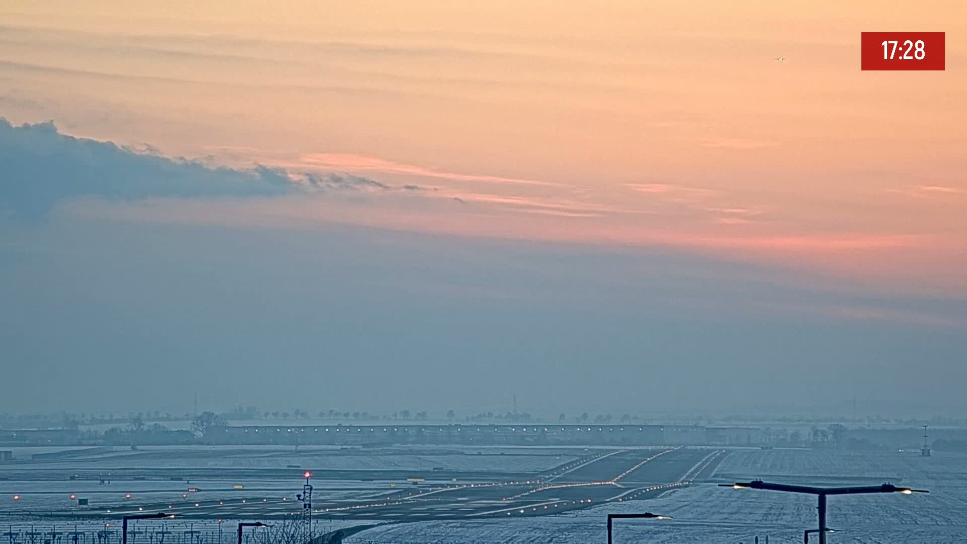 A snow-covered airport runway is visible under a hazy, pinkish sunset.