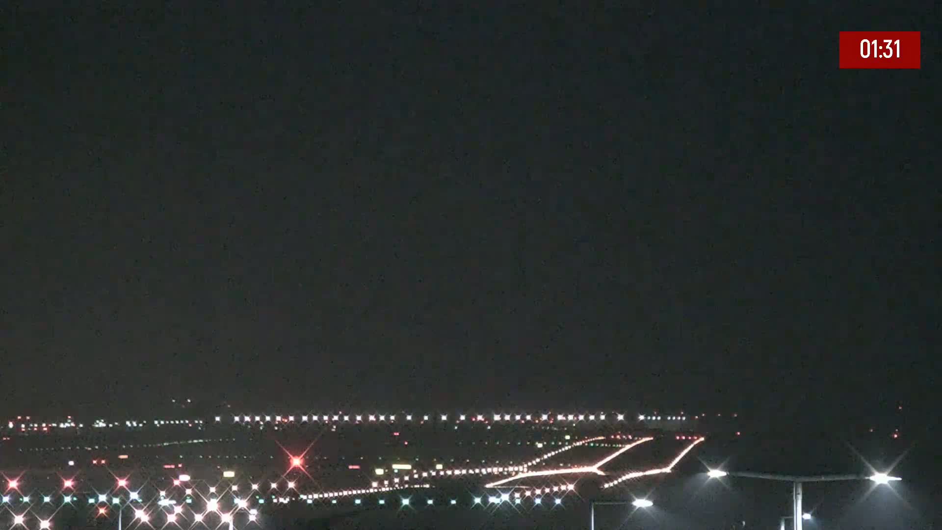 A nighttime view of an airport runway illuminated with lights under a clear, dark sky.