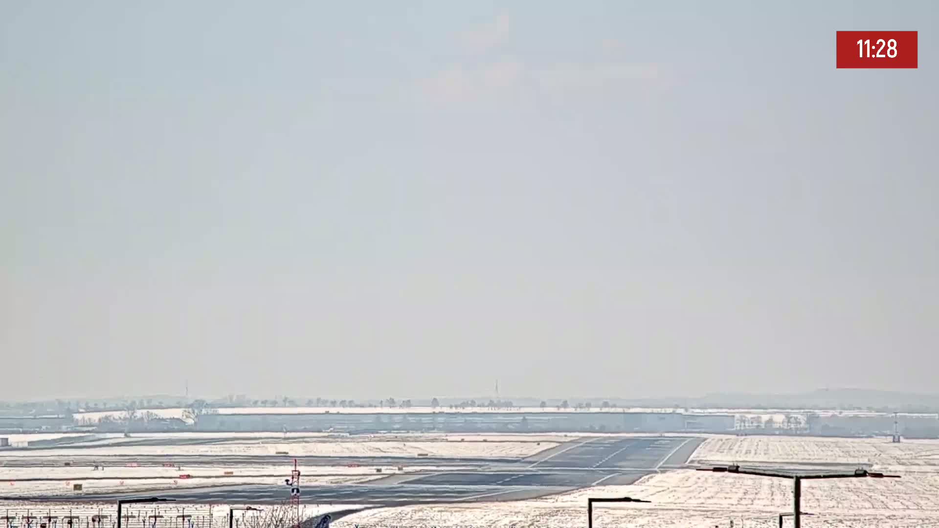 A snow-covered airport runway stretches into the hazy distance under a bright, clear sky.