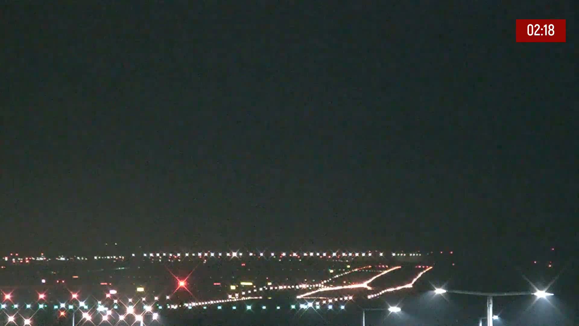 A nighttime long shot of an airport runway illuminated by lights under a clear, dark sky.