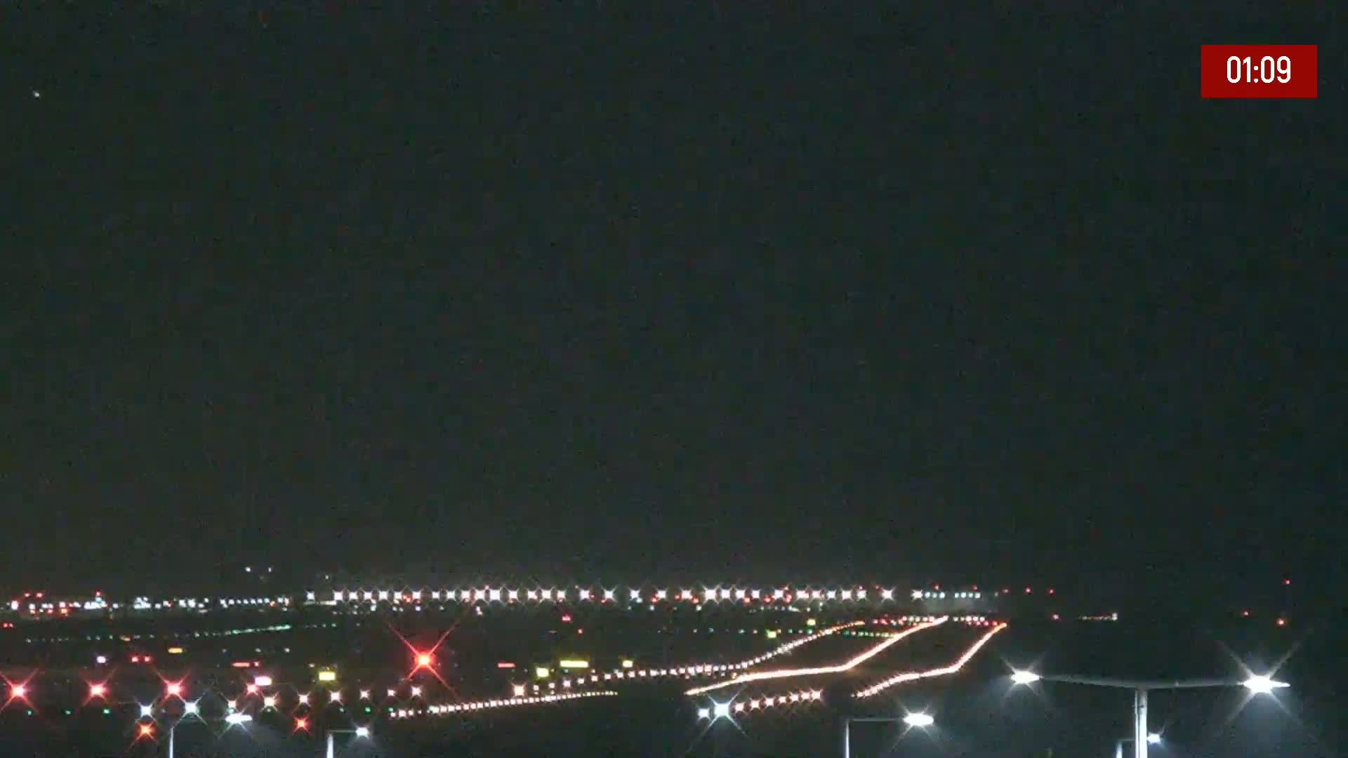 A nighttime view of brightly lit airport runways and taxiways under a clear, dark sky.