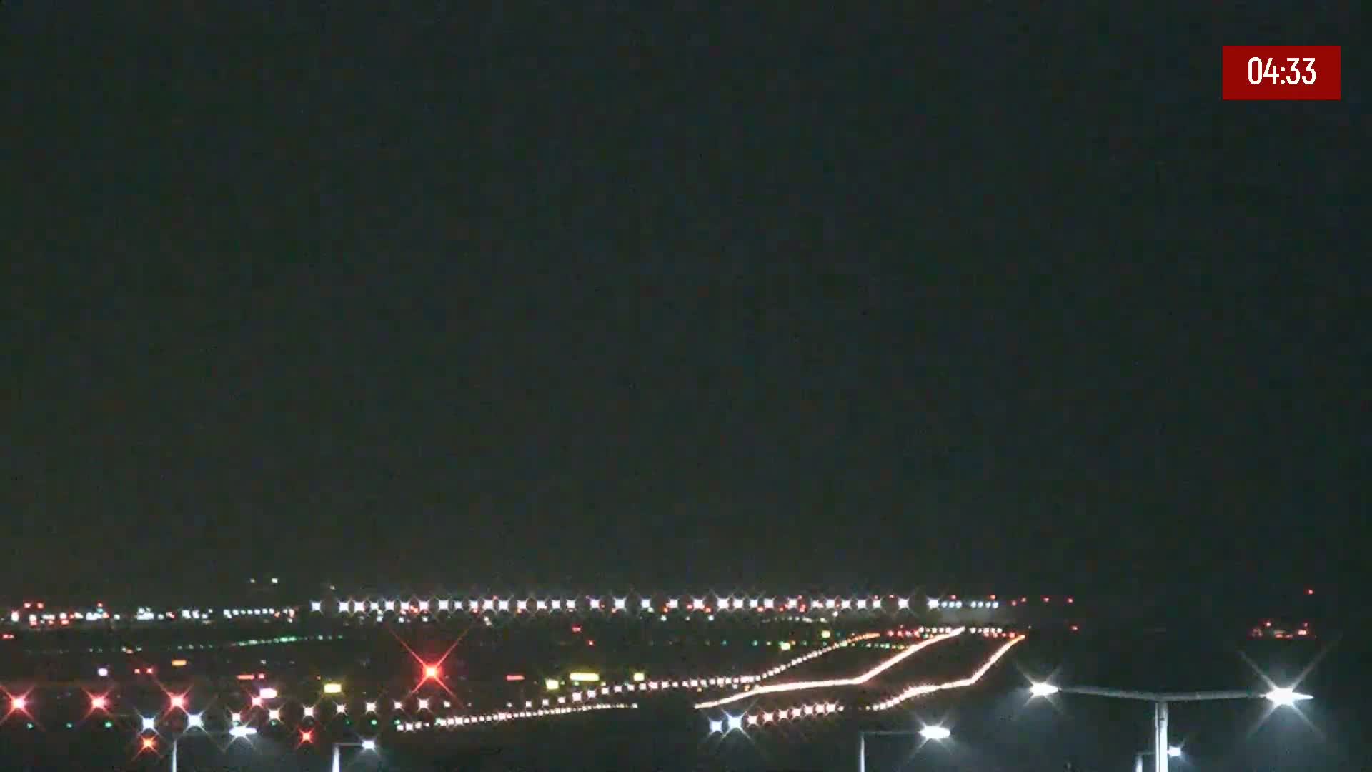 A nighttime long shot of an airport runway with its lights illuminated under a clear, dark sky.