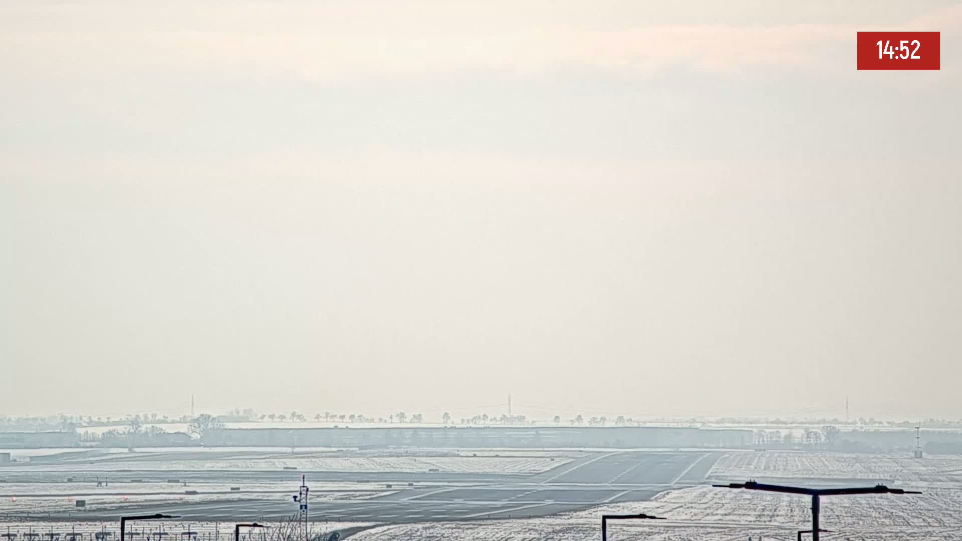 A hazy, overcast view of a snow-covered airport runway and surrounding landscape.