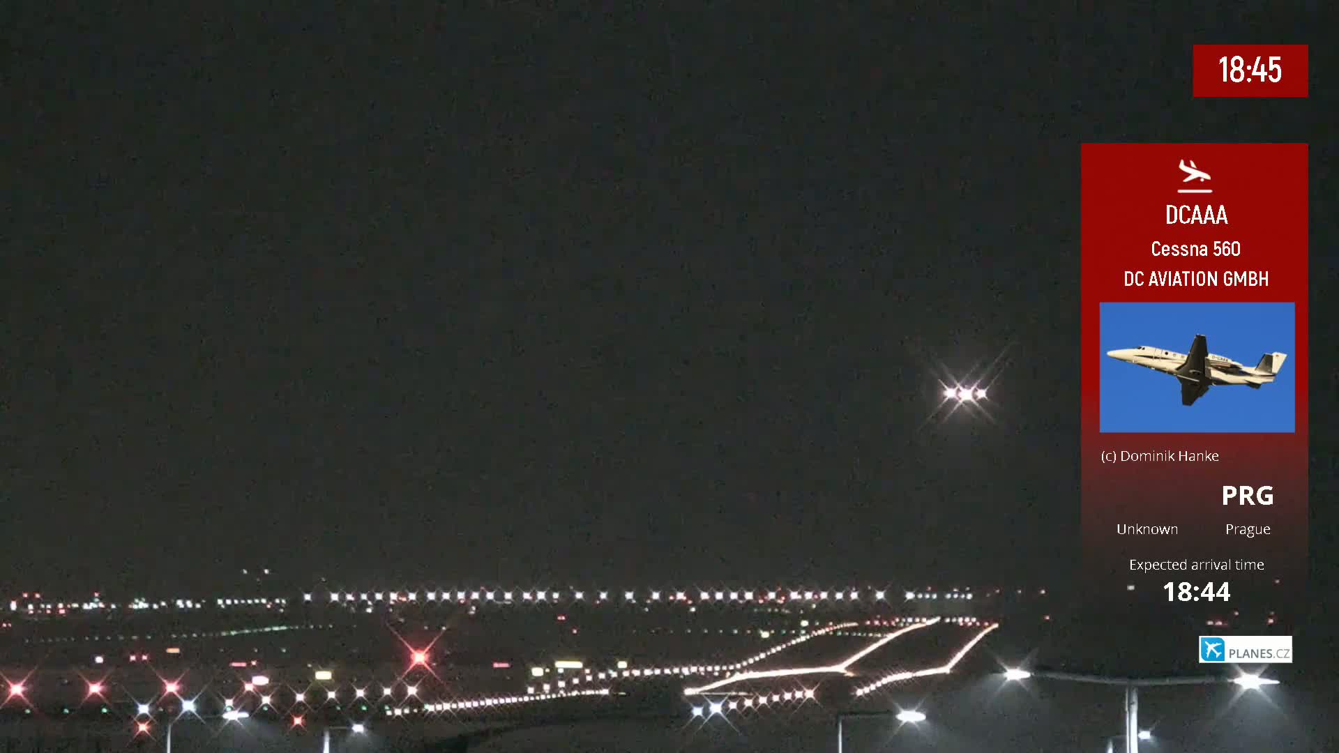 A nighttime view of an airport runway with lights illuminated, under a dark sky.