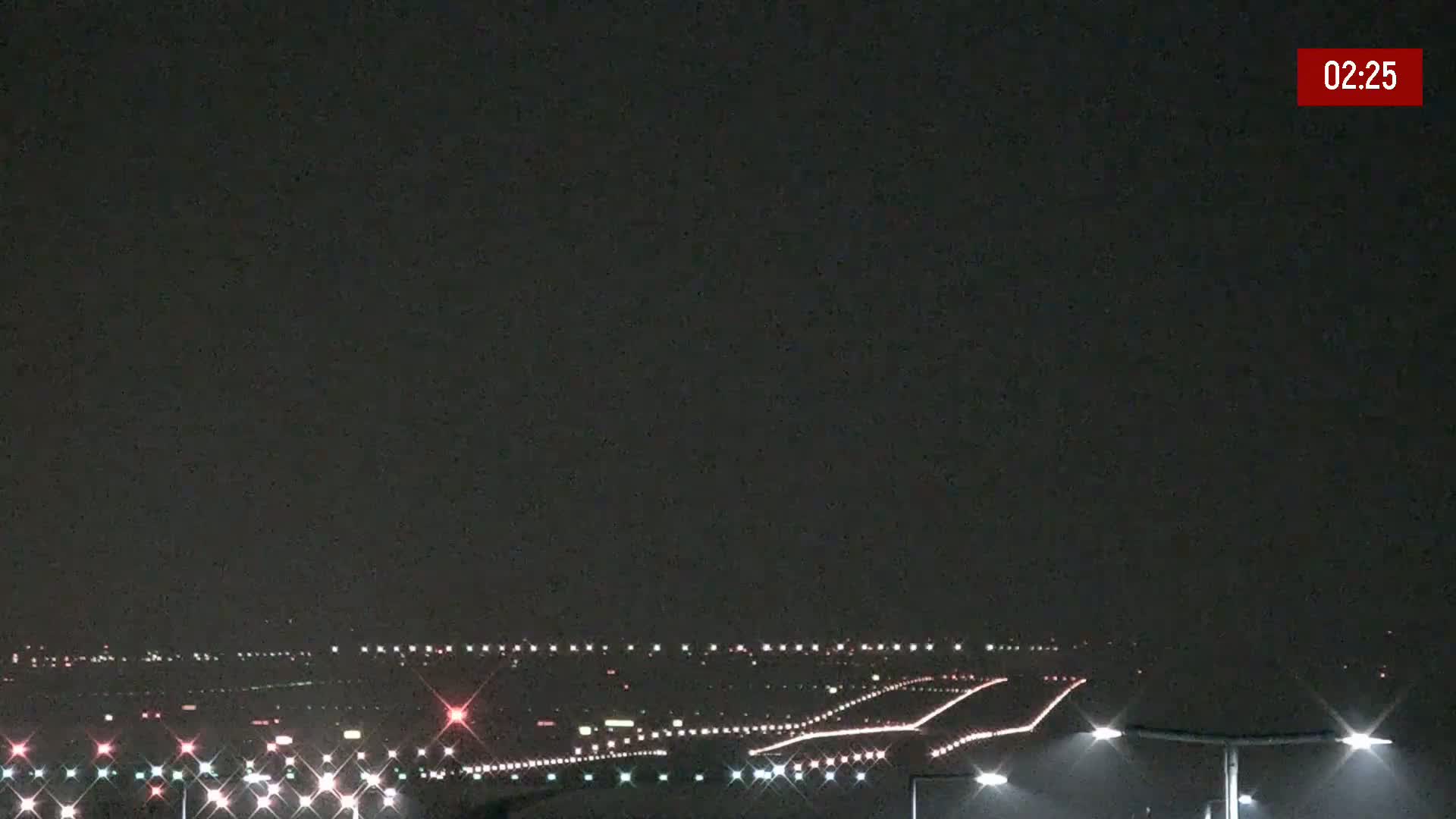 A nighttime view of an airport runway illuminated with lights under a dark sky.
