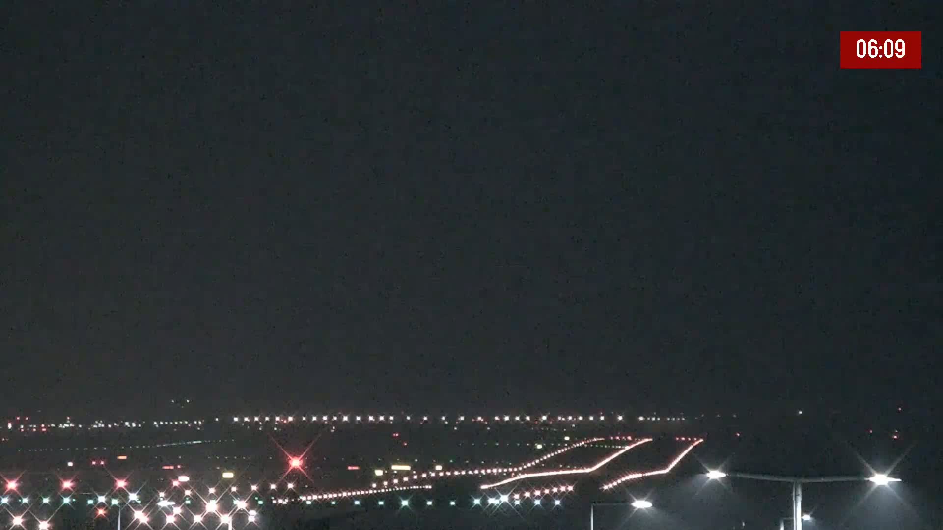 Under a dark night sky, illuminated runway lights stretch across a flat landscape.