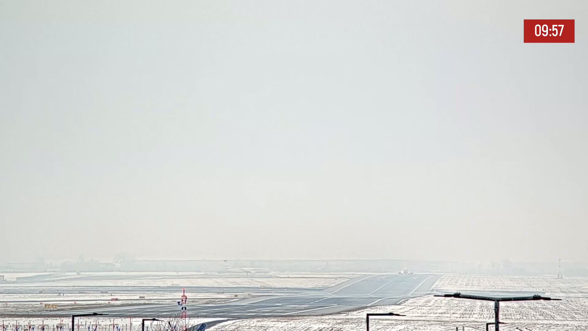A hazy, snowy airport runway stretches into the distance under a pale sky.