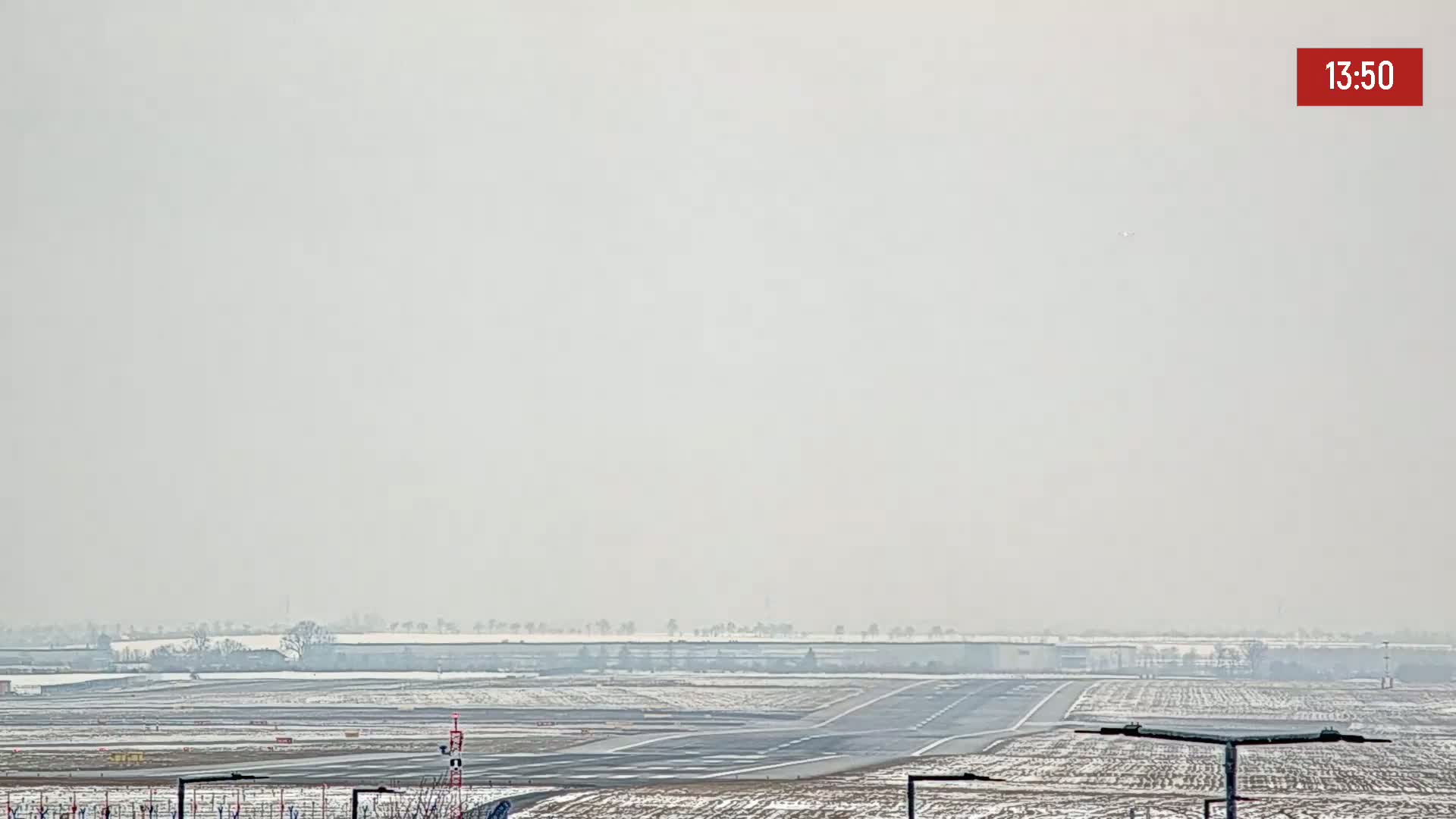 A hazy, snowy airport runway and surrounding fields are visible under a gray sky.