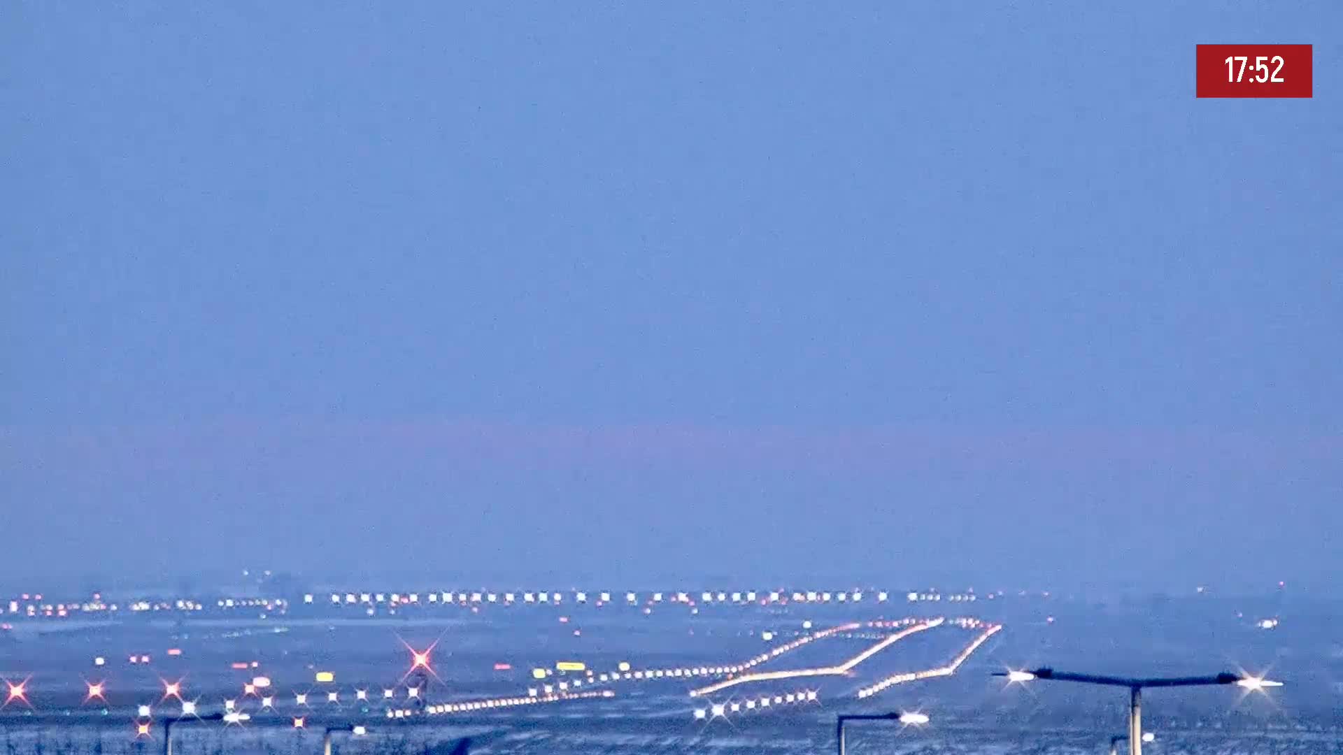 A long runway with lights illuminated at dusk or dawn under a clear, pale blue sky.