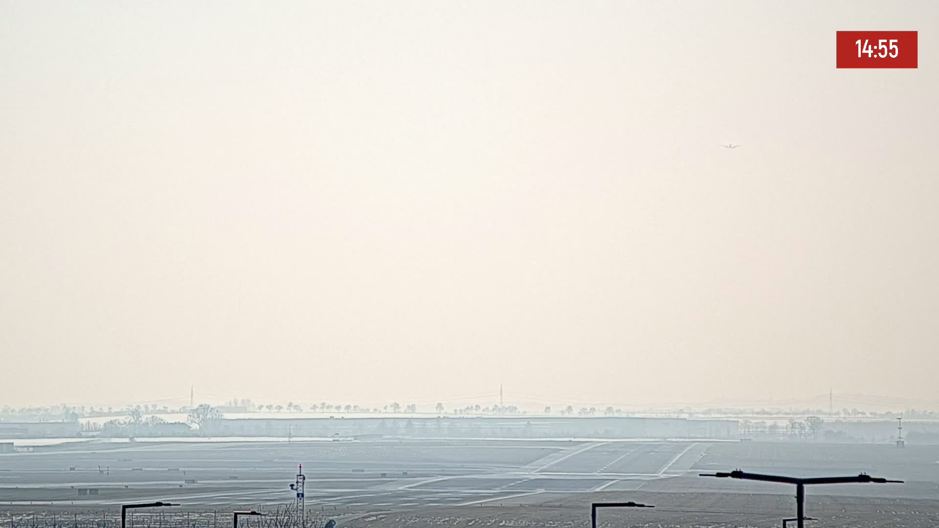 A hazy view of an airport runway and surrounding flat land, with a single airplane visible in the distance.