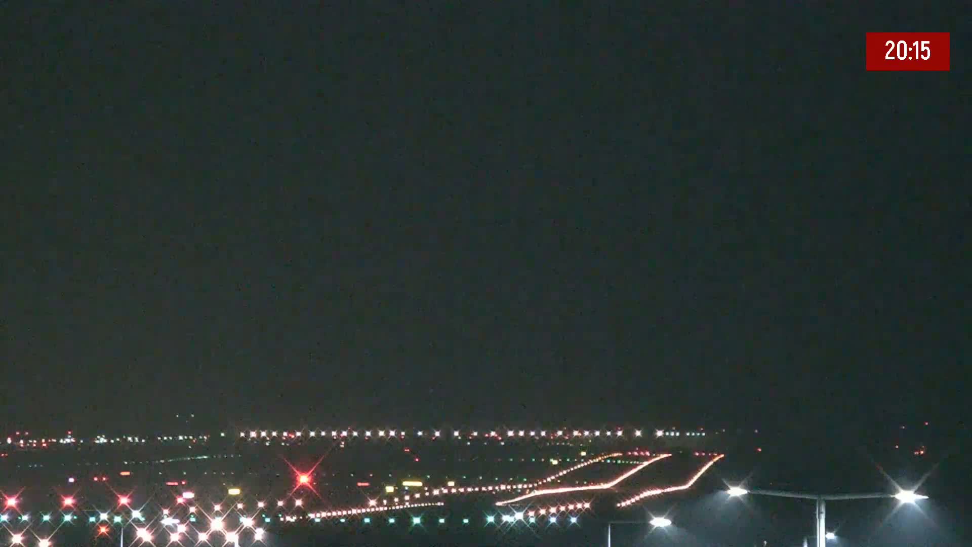 A nighttime view of an airport runway illuminated with lights under a clear, dark sky.
