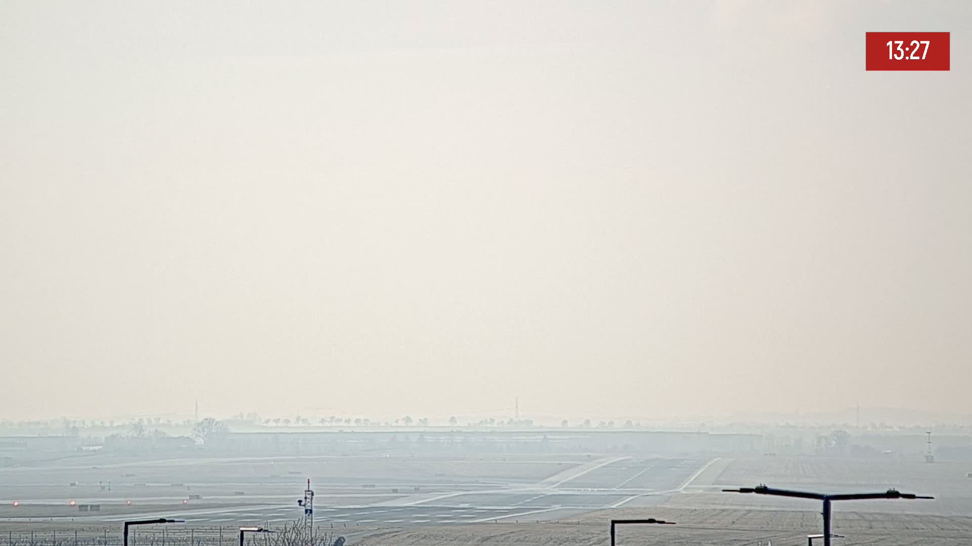 A hazy view of an airport runway and surrounding flat land is visible under a light overcast sky.