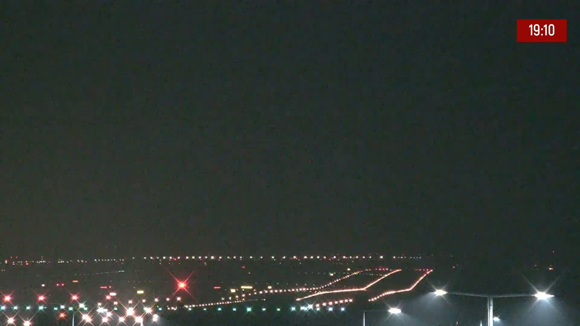A nighttime view of an airport runway with its lights illuminated under a dark sky.