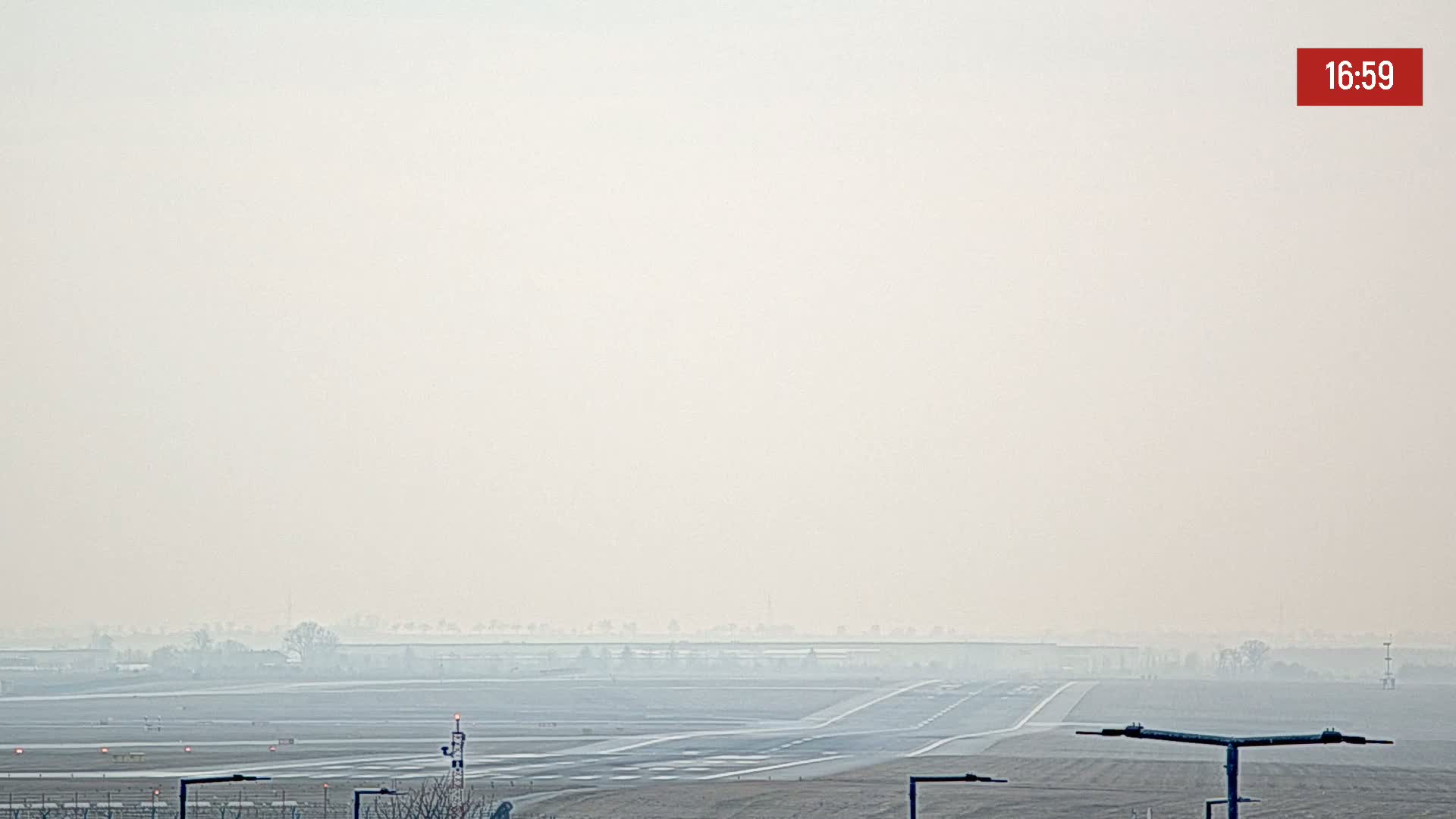 A hazy view of an airport runway and surrounding flat land under a light, overcast sky.