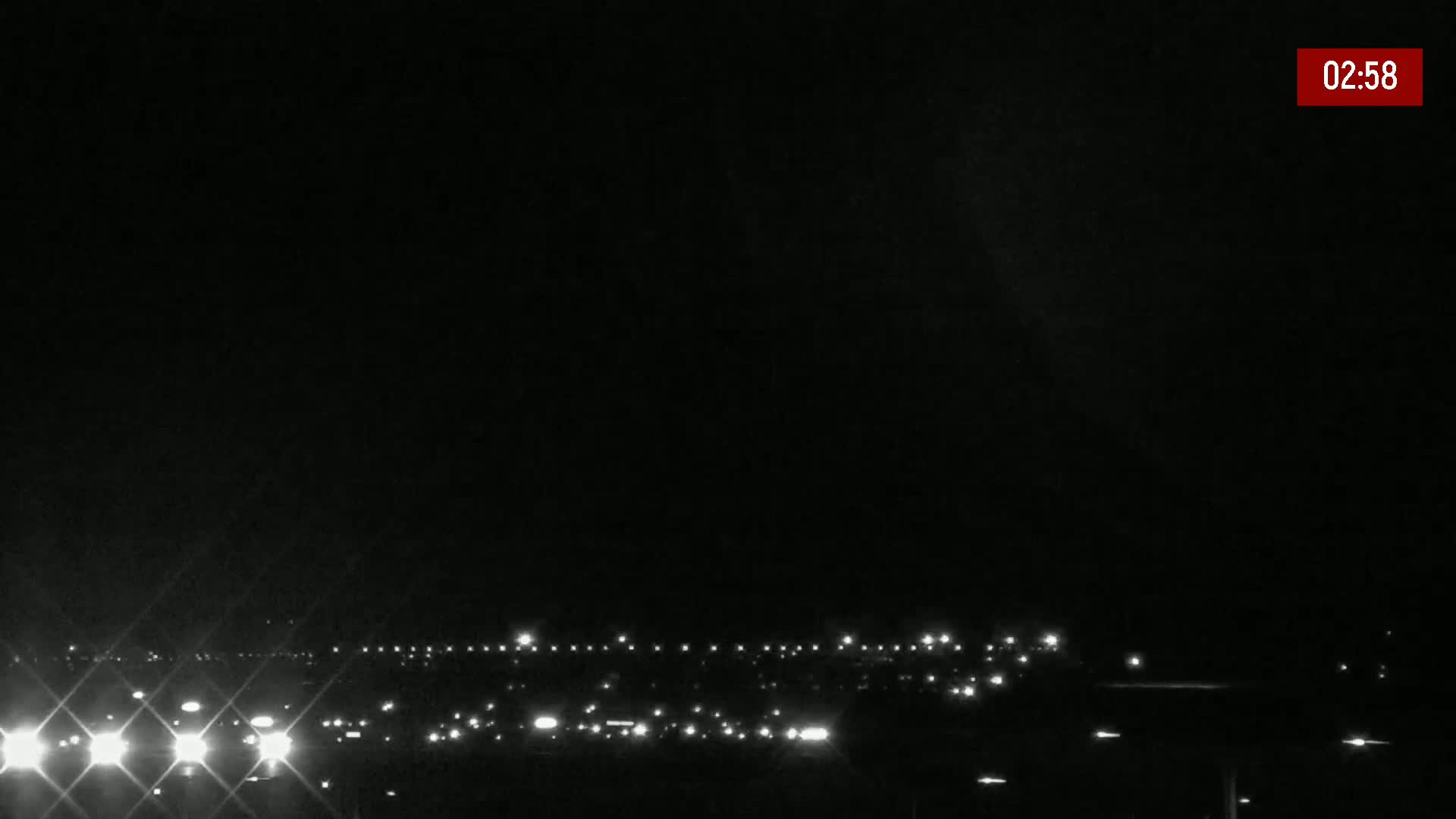 Under a dark night sky, a distant line of headlights from vehicles is visible on a roadway.