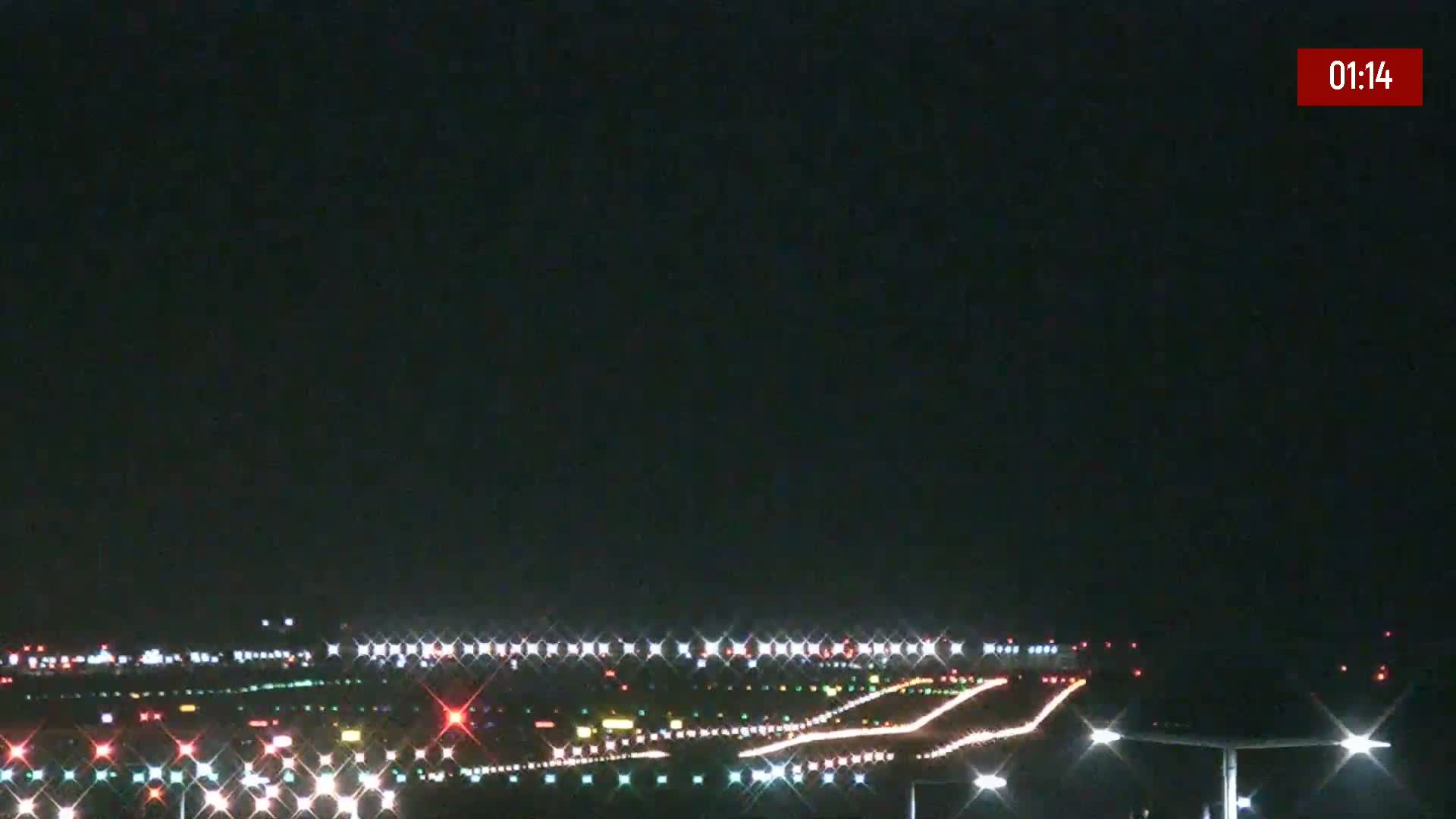 A nighttime long shot of an airport runway illuminated with lights under a clear, dark sky.