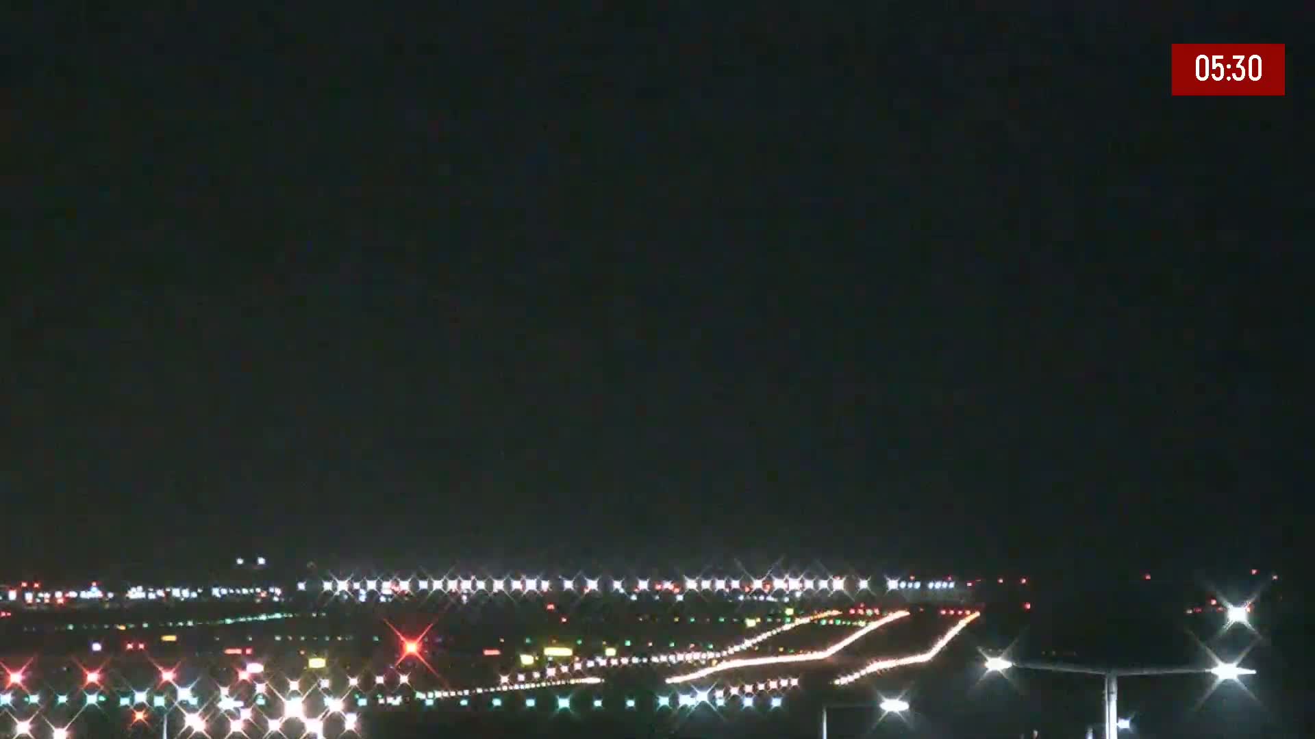 A nighttime view of an airport runway illuminated by bright lights under a clear, dark sky.