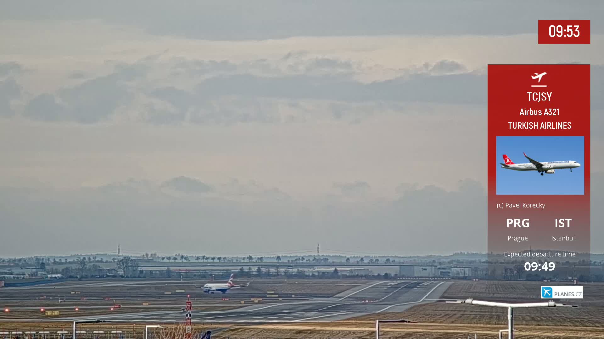 A wide shot of an airport runway on an overcast day shows two airplanes, one taking off and another taxiing.