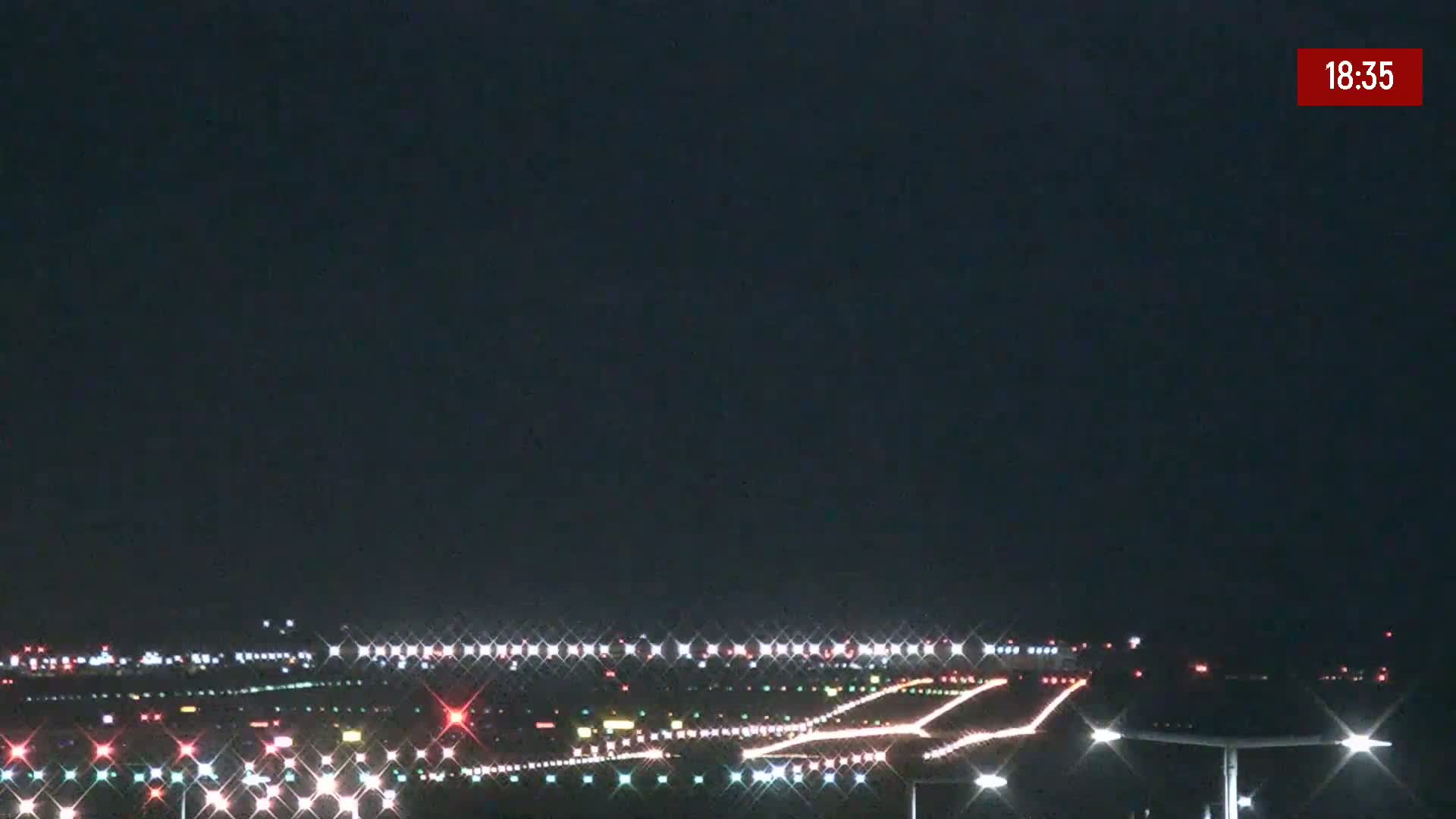 A nighttime view of an airport runway illuminated with lights under a dark sky.