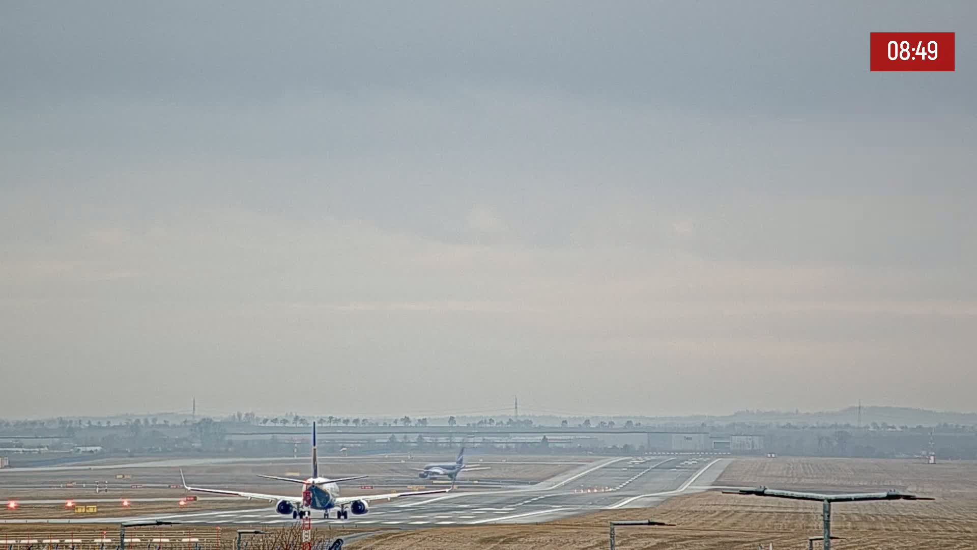An airplane is landing on a runway at an airport under an overcast sky.