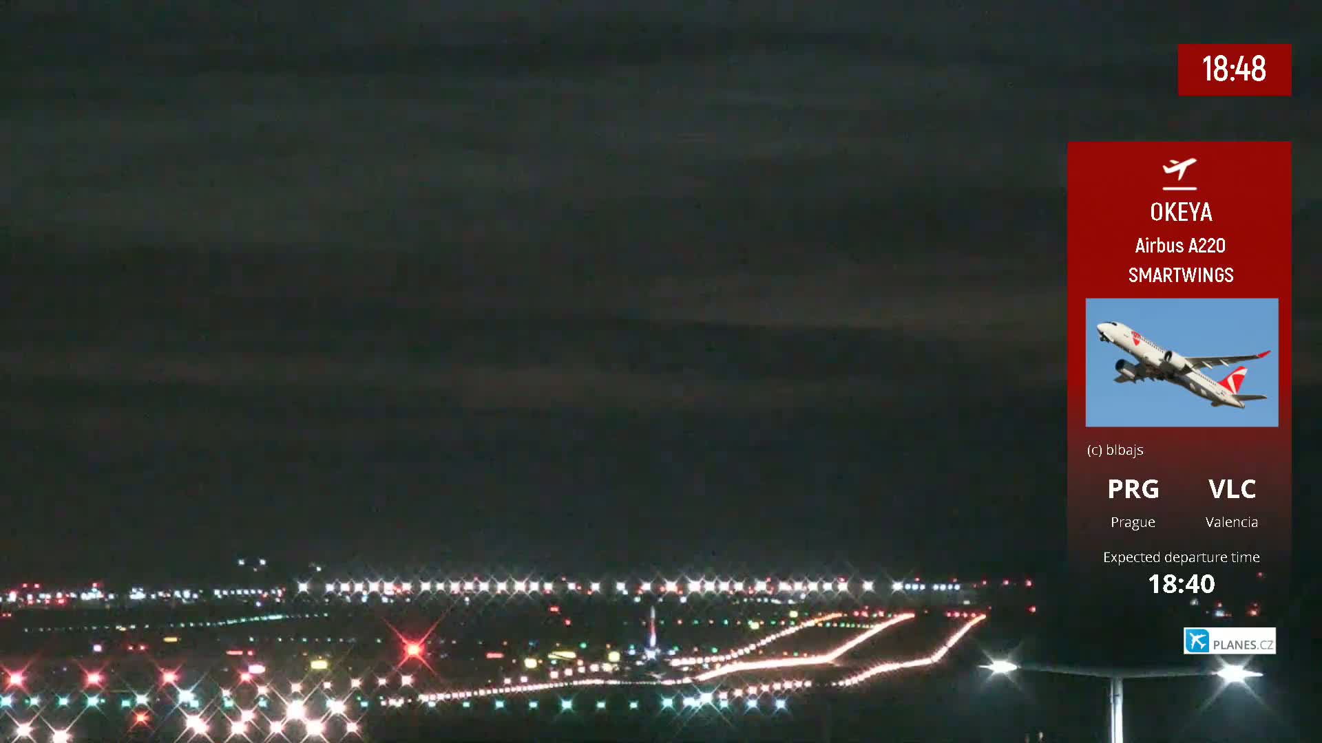 A Smartwings Airbus A220 airplane is taking off at night from a brightly lit runway.