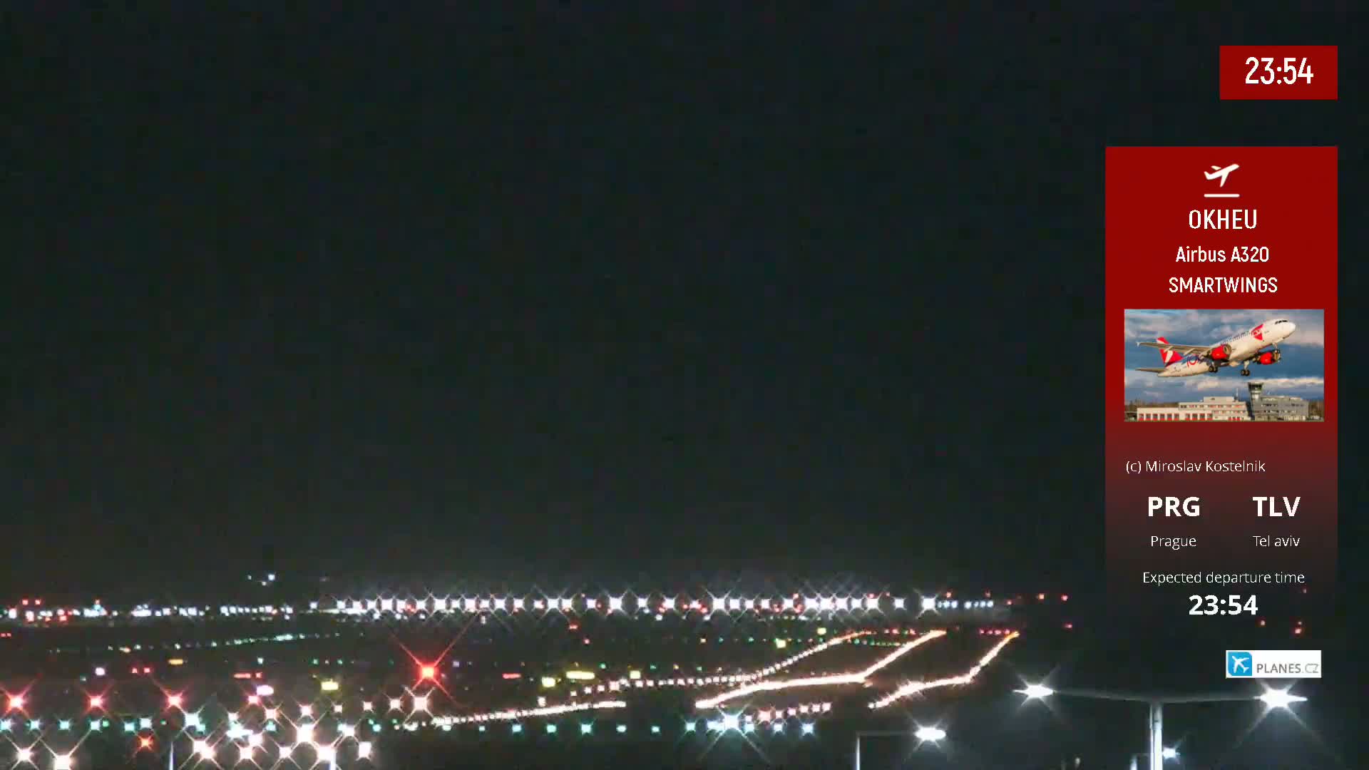 A nighttime, brightly lit airport runway is shown with an airplane taking off in the background.