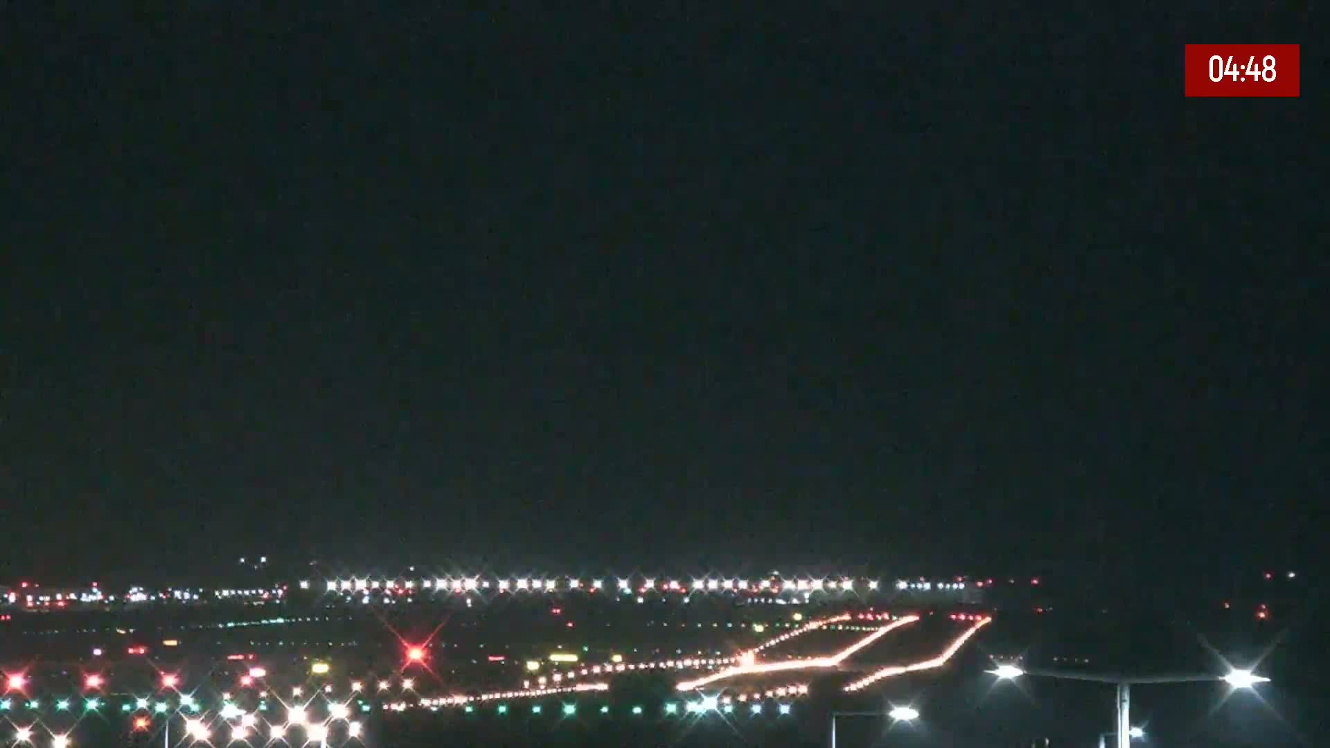 A nighttime long shot of an airport runway illuminated with lights under a clear, dark sky.
