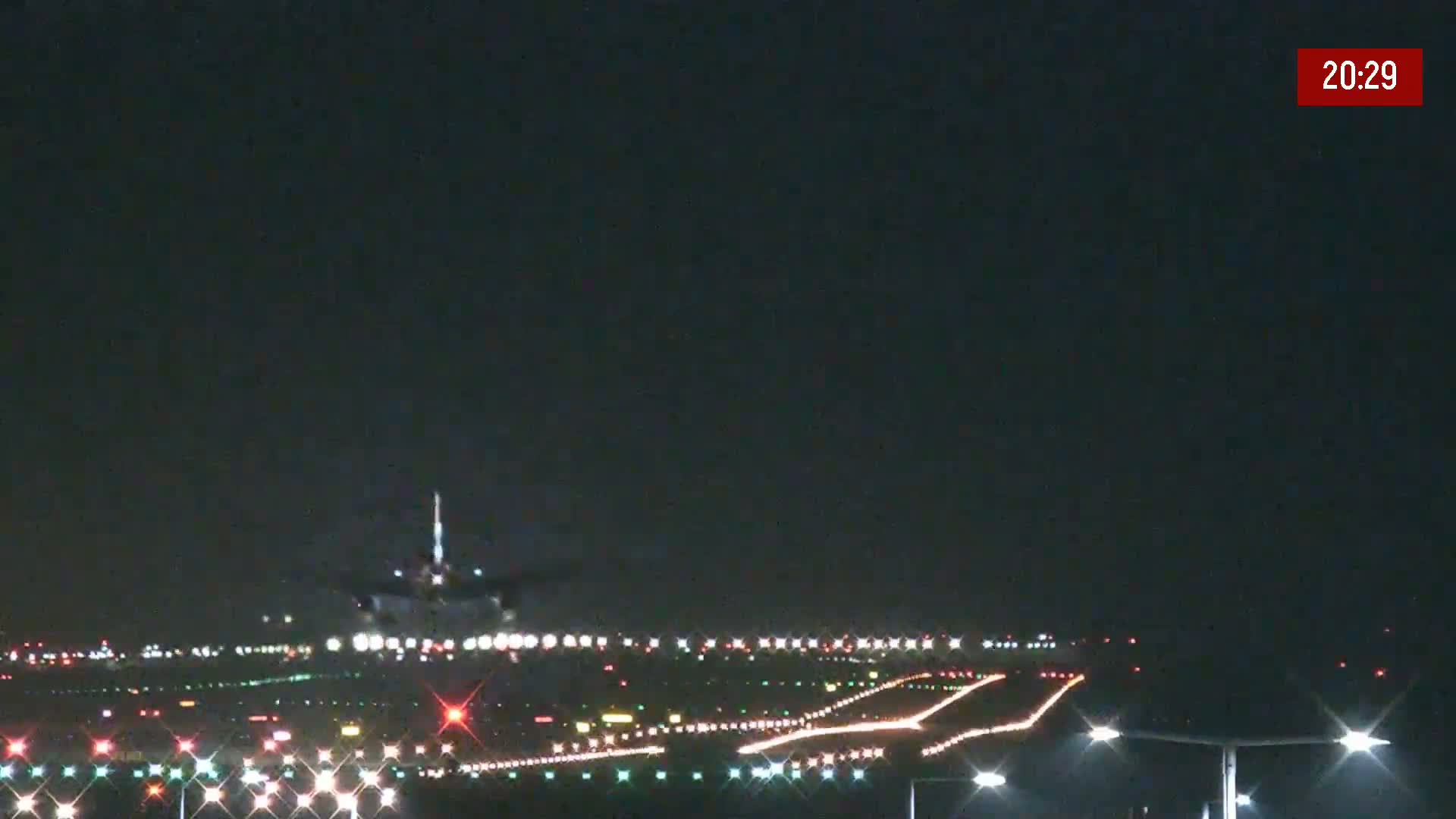 At night, an airplane is landing on a runway surrounded by illuminated lights.