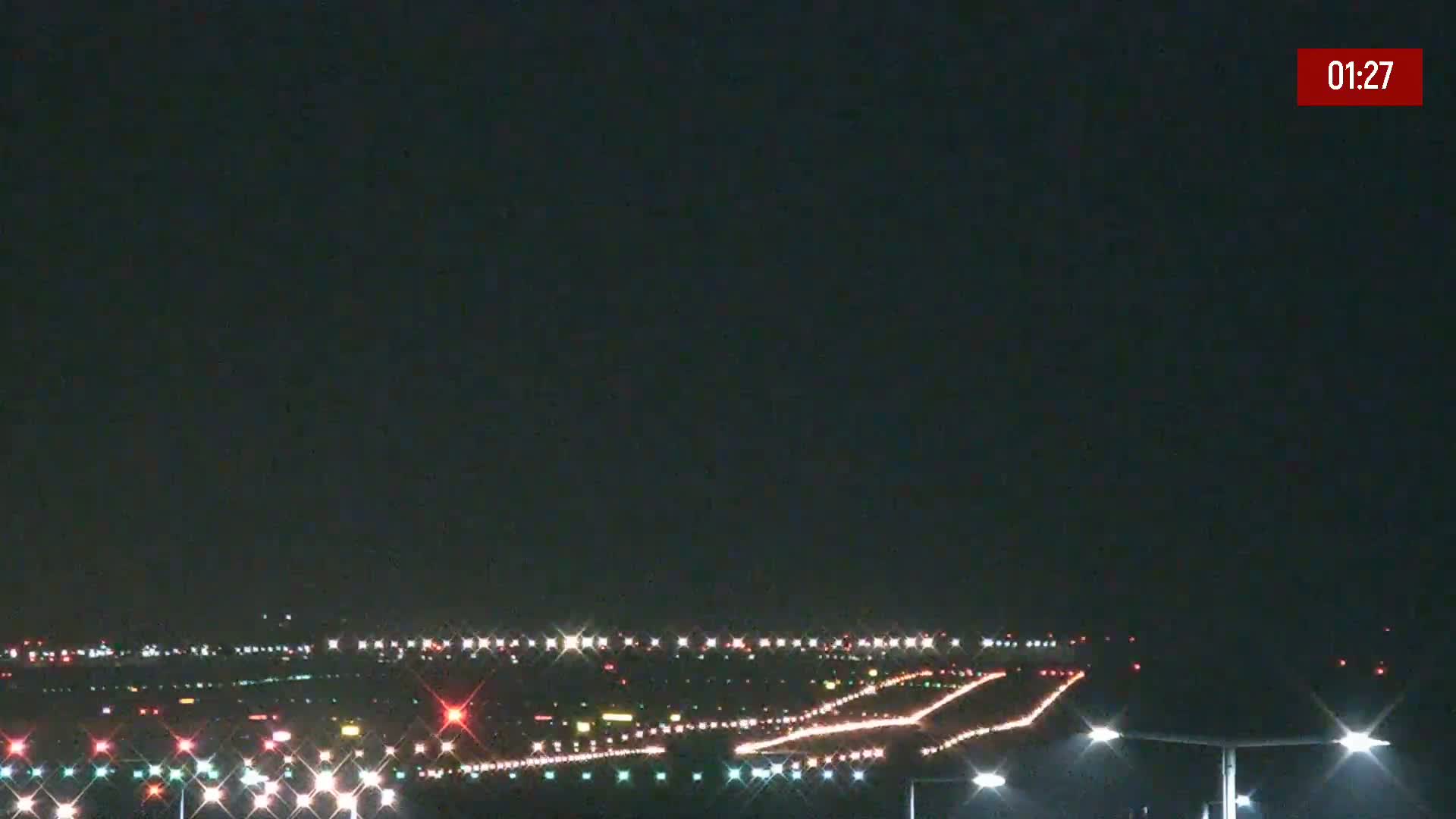 At night, the brightly lit runway and taxiways of an airport are visible under a clear, dark sky.
