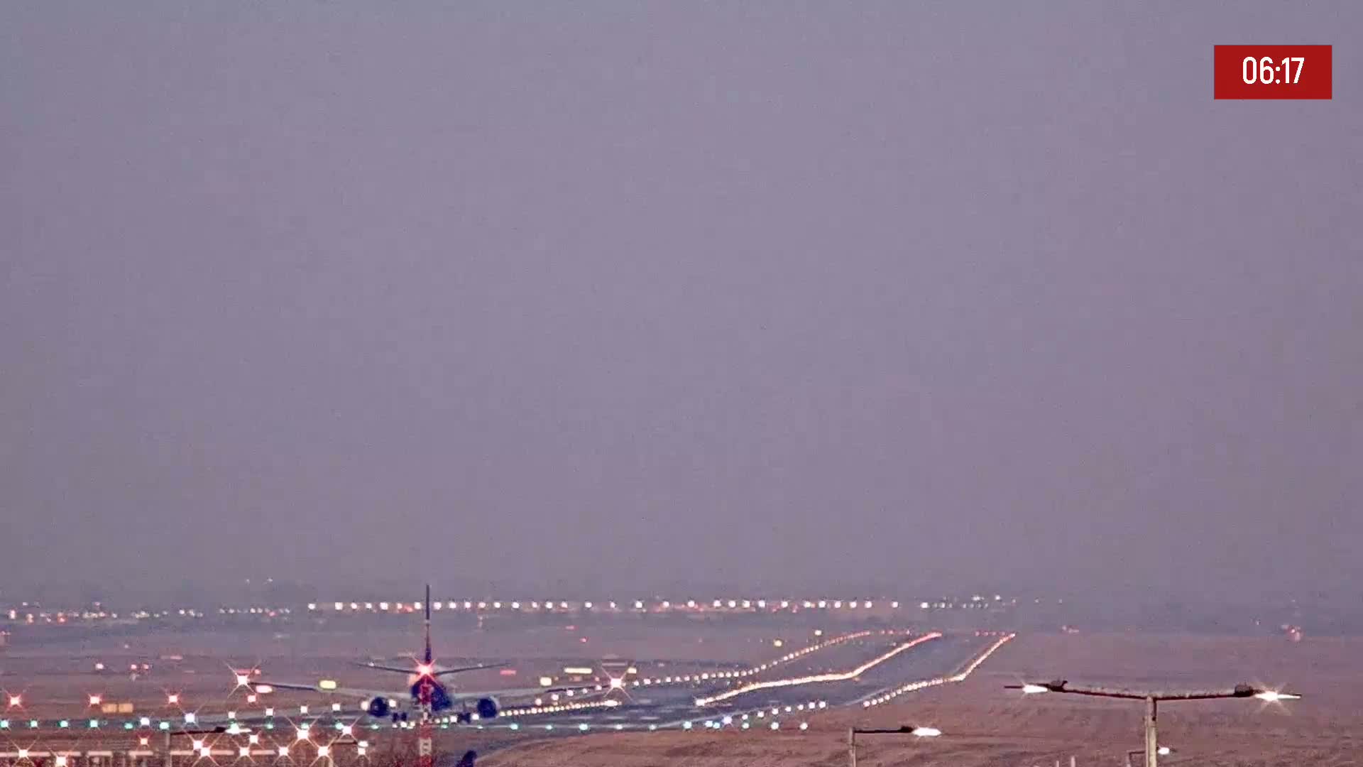 A plane taxis on a runway at an airport under a hazy, pale-purple sky.