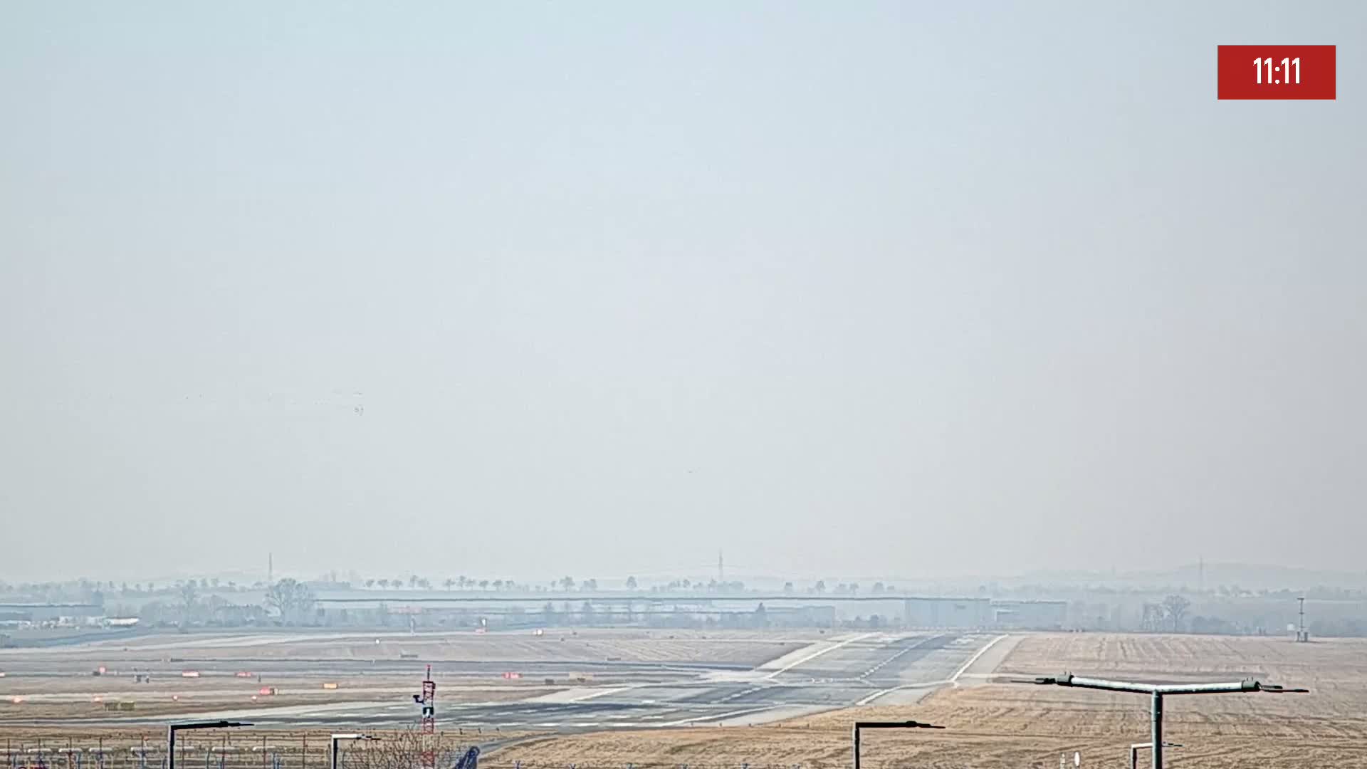A hazy view of an airport runway and surrounding flat land under a light-grey sky.