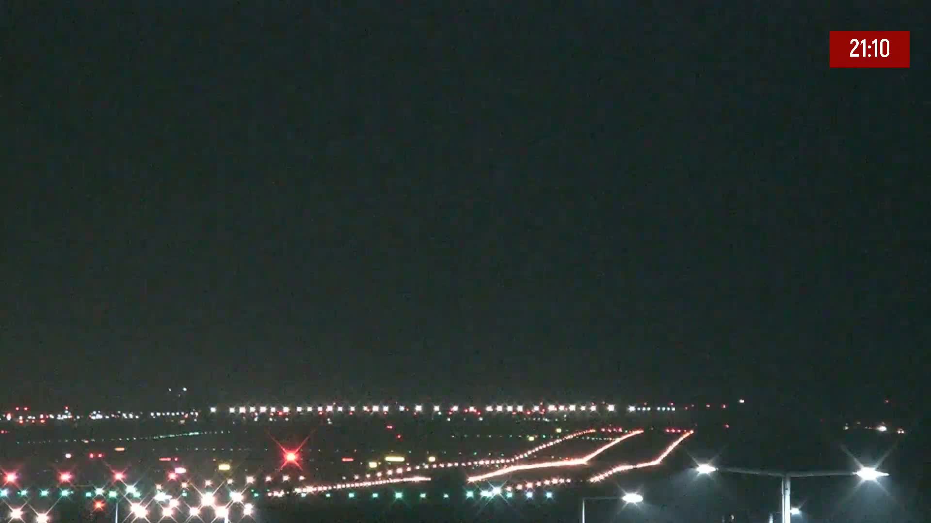 A nighttime view of an airport runway with its lights illuminated under a dark sky.