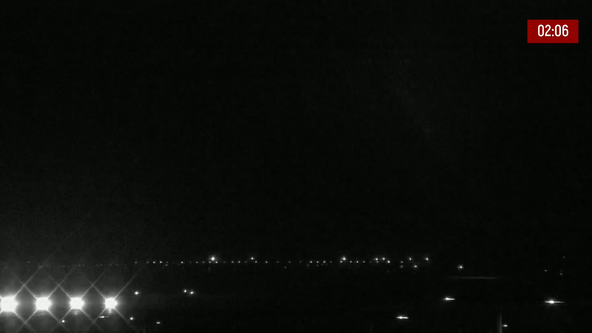 A nighttime, dark scene shows a distant line of lights on the horizon under a clear, black sky.