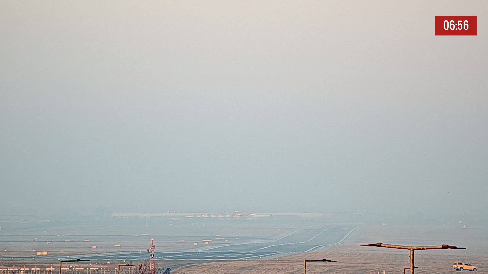 A hazy view of an airport runway and surrounding landscape is visible in the early morning.