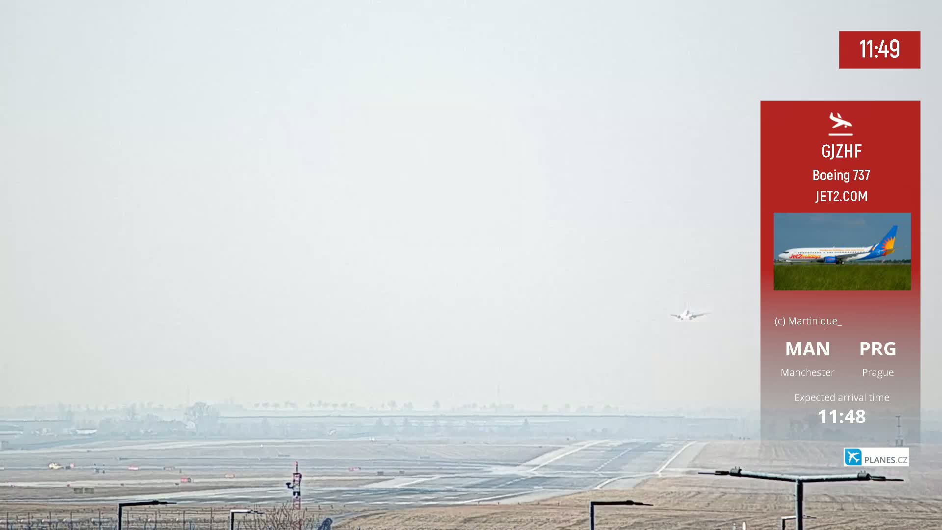 A hazy view of an airport runway shows a small plane in the distance, with another plane visible in the far background.