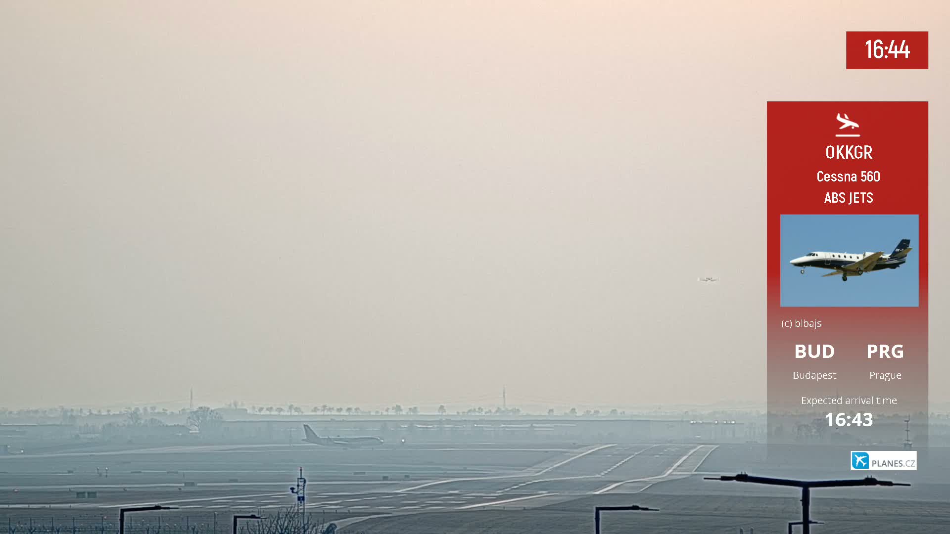 A hazy airport runway is visible with a small private jet in the distance.