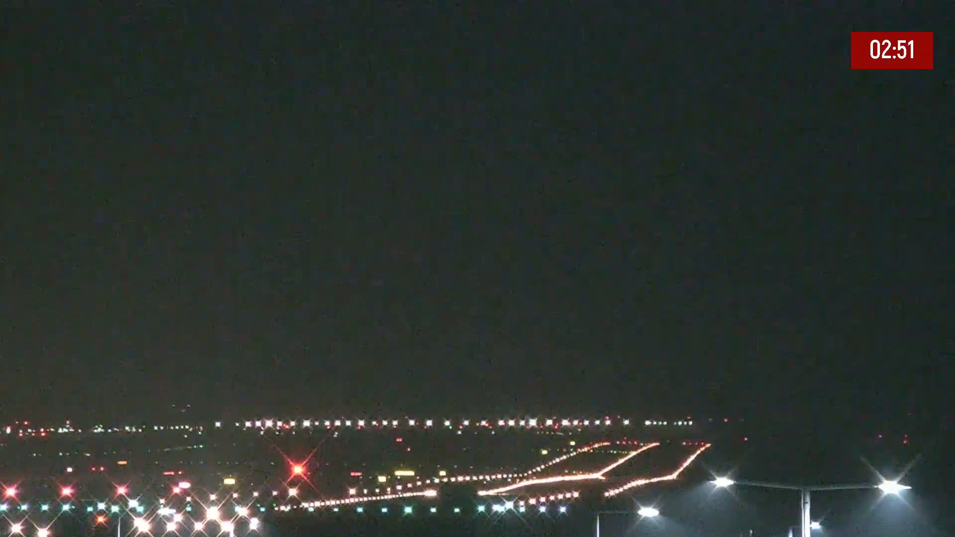 A nighttime long shot of an airport runway illuminated by lights under a clear, dark sky.