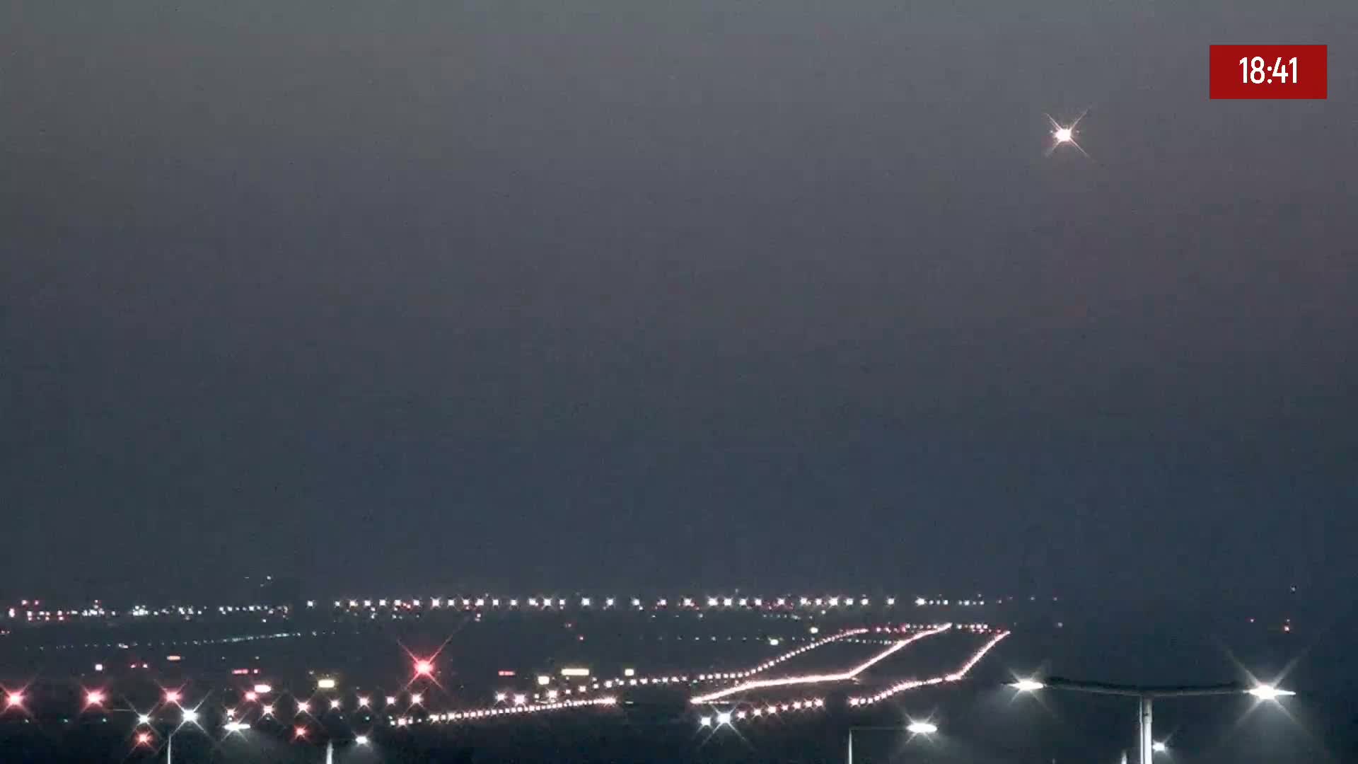 A nighttime long shot shows a bright star in a hazy sky above a distant highway and city lights.