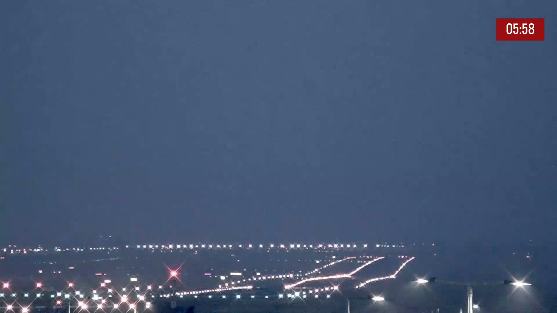 Under a dark, twilight sky, a multi-lane highway stretches into the distance, dotted with the lights of numerous vehicles.