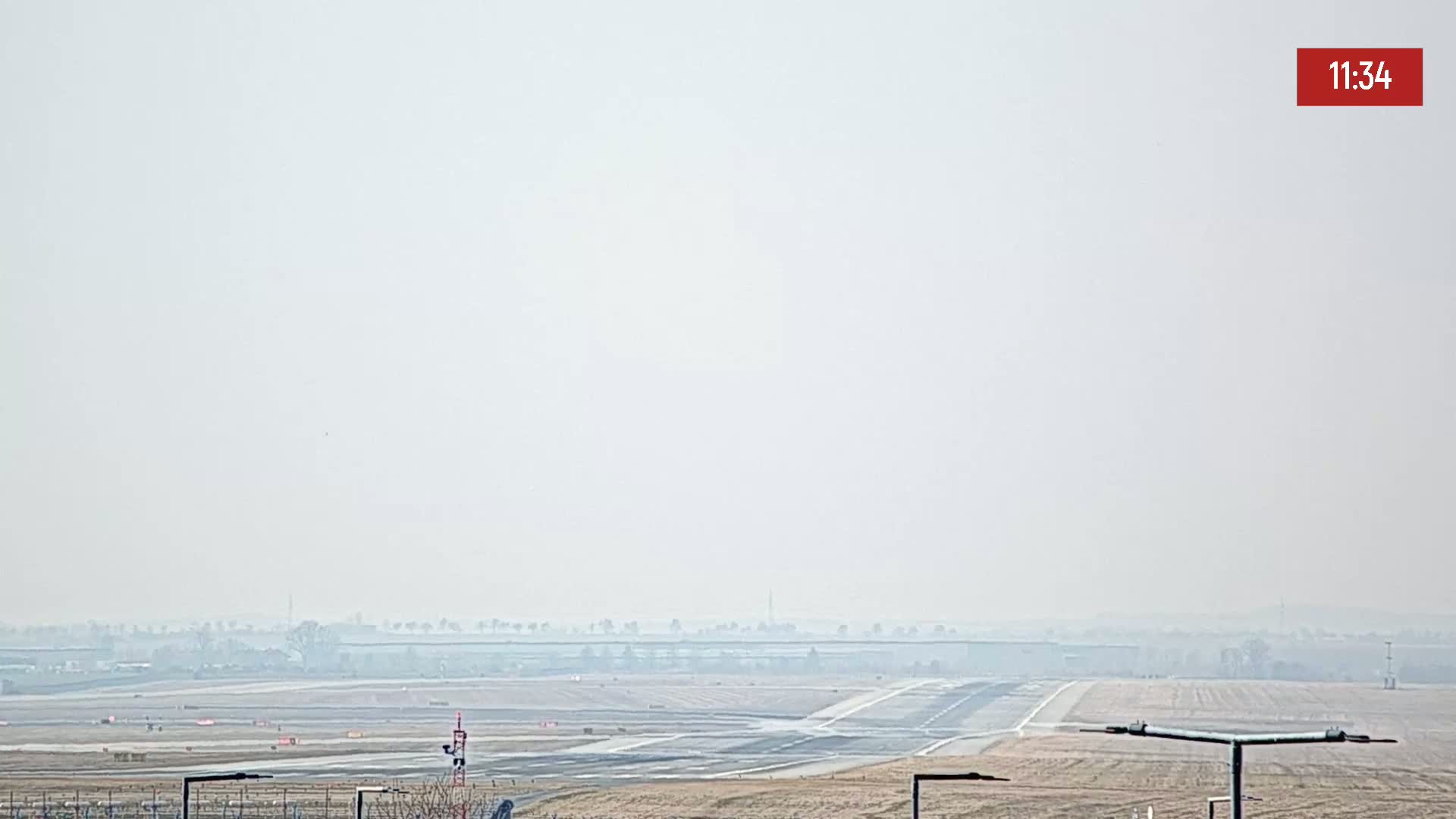 A hazy view of an airport runway and surrounding flat land under a light-grey sky.