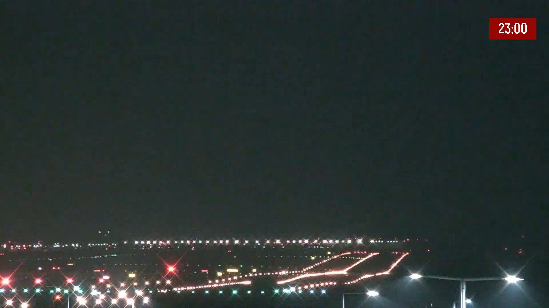 A nighttime view of an airport runway illuminated with lights under a dark, clear sky.