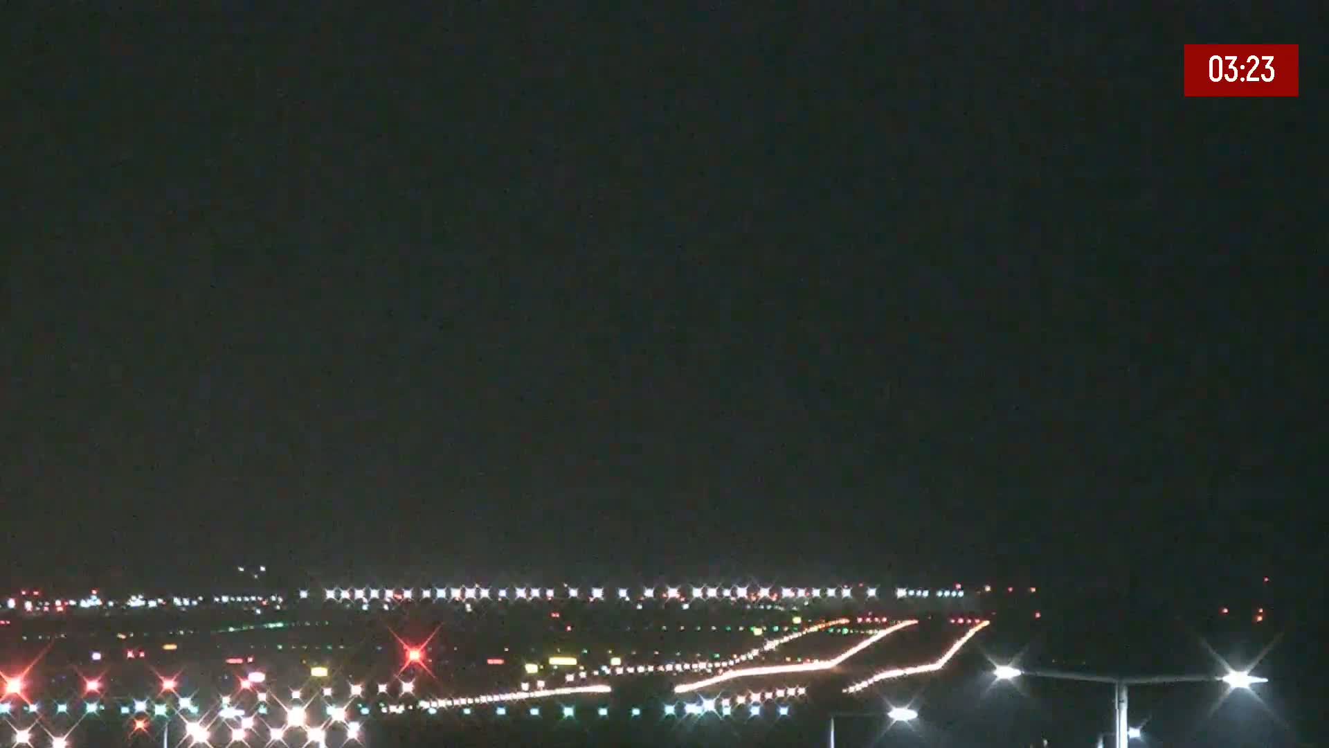 A nighttime long shot of an airport runway with lights illuminating the tarmac under a clear, dark sky.