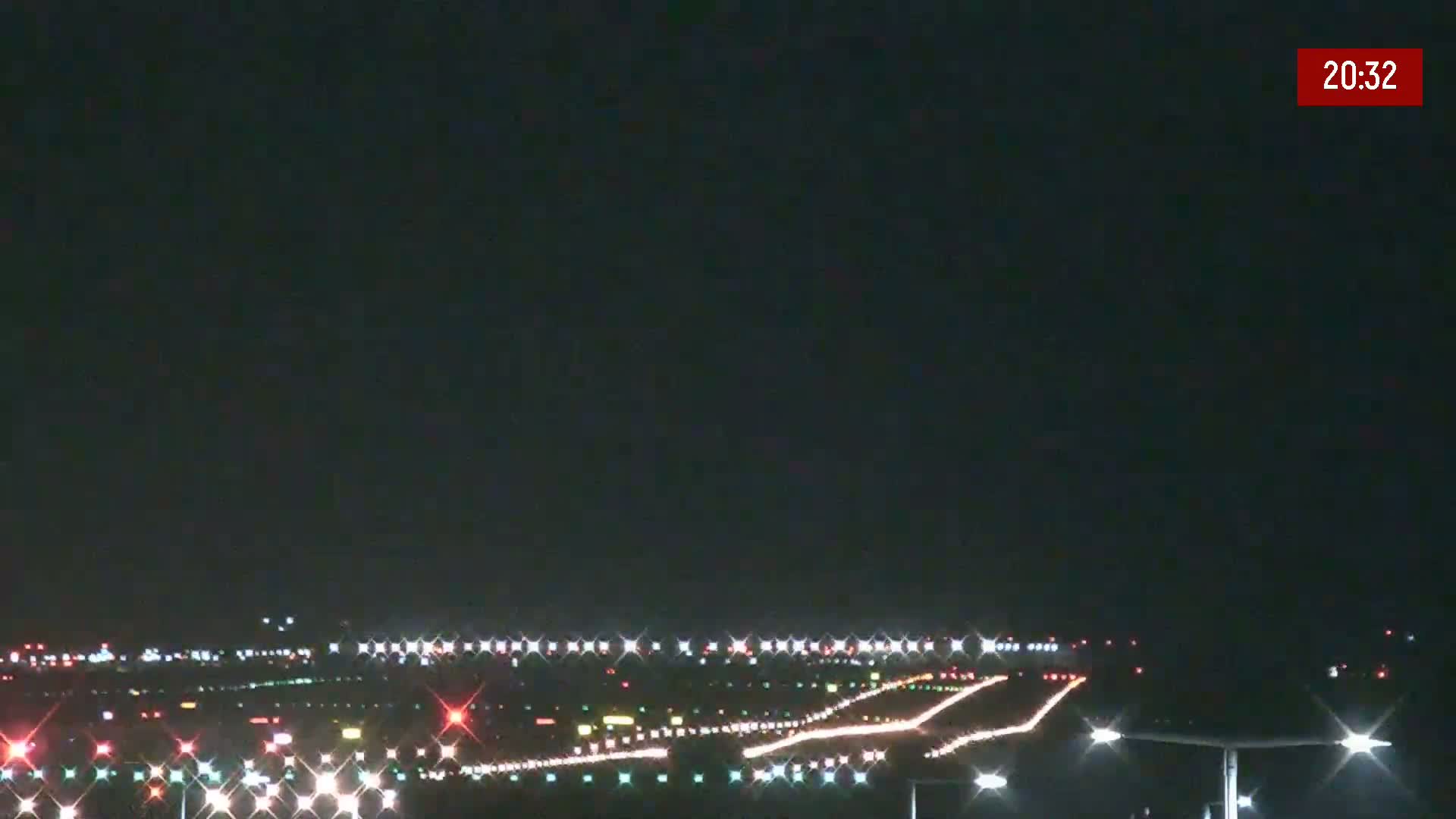 A nighttime view of an airport runway illuminated by numerous lights under a clear, dark sky.