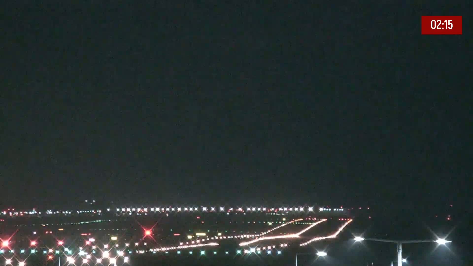A nighttime long shot of an airport runway illuminated with lights under a dark sky.