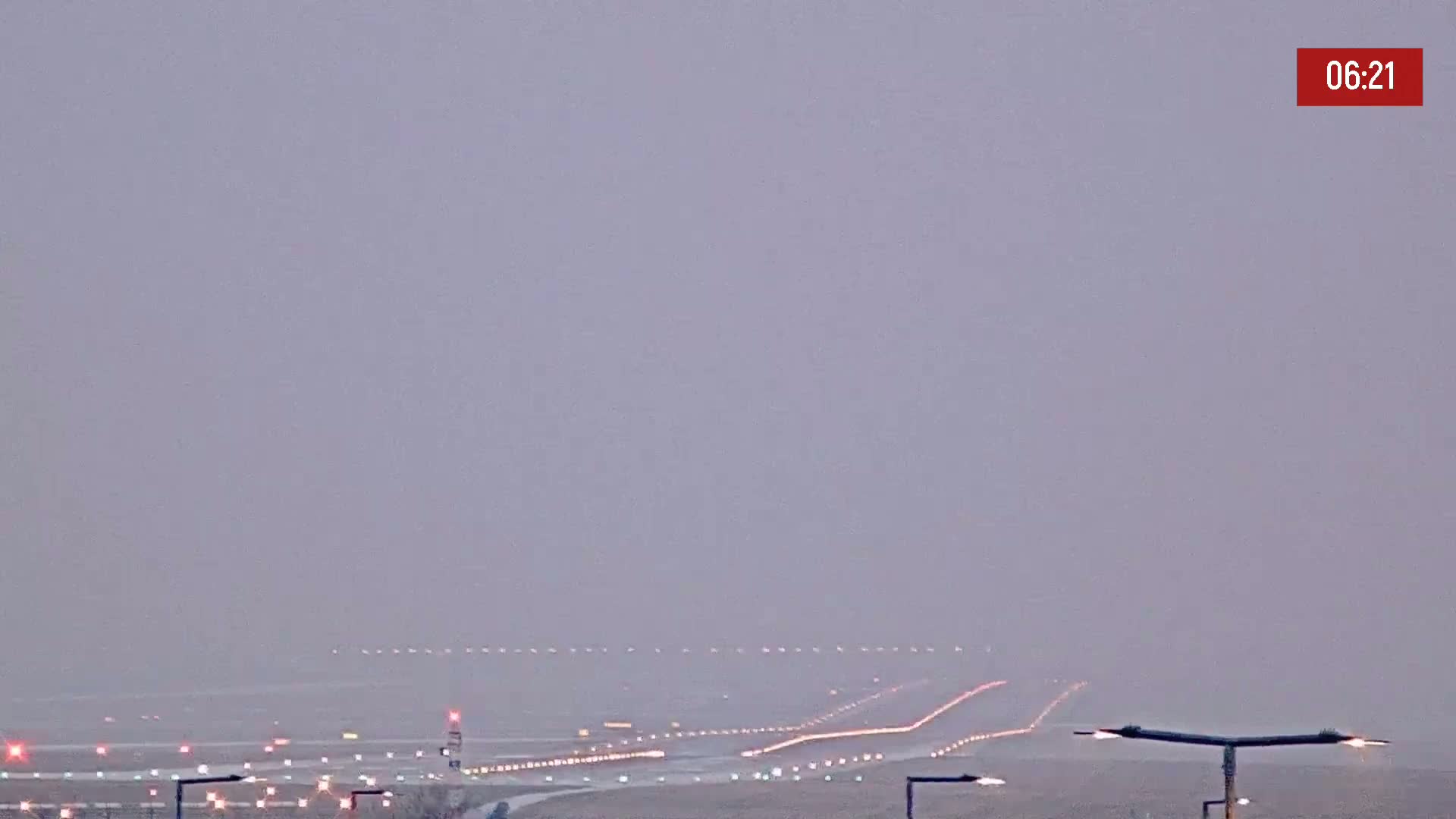 A long runway with lights is visible through a hazy, overcast sky.