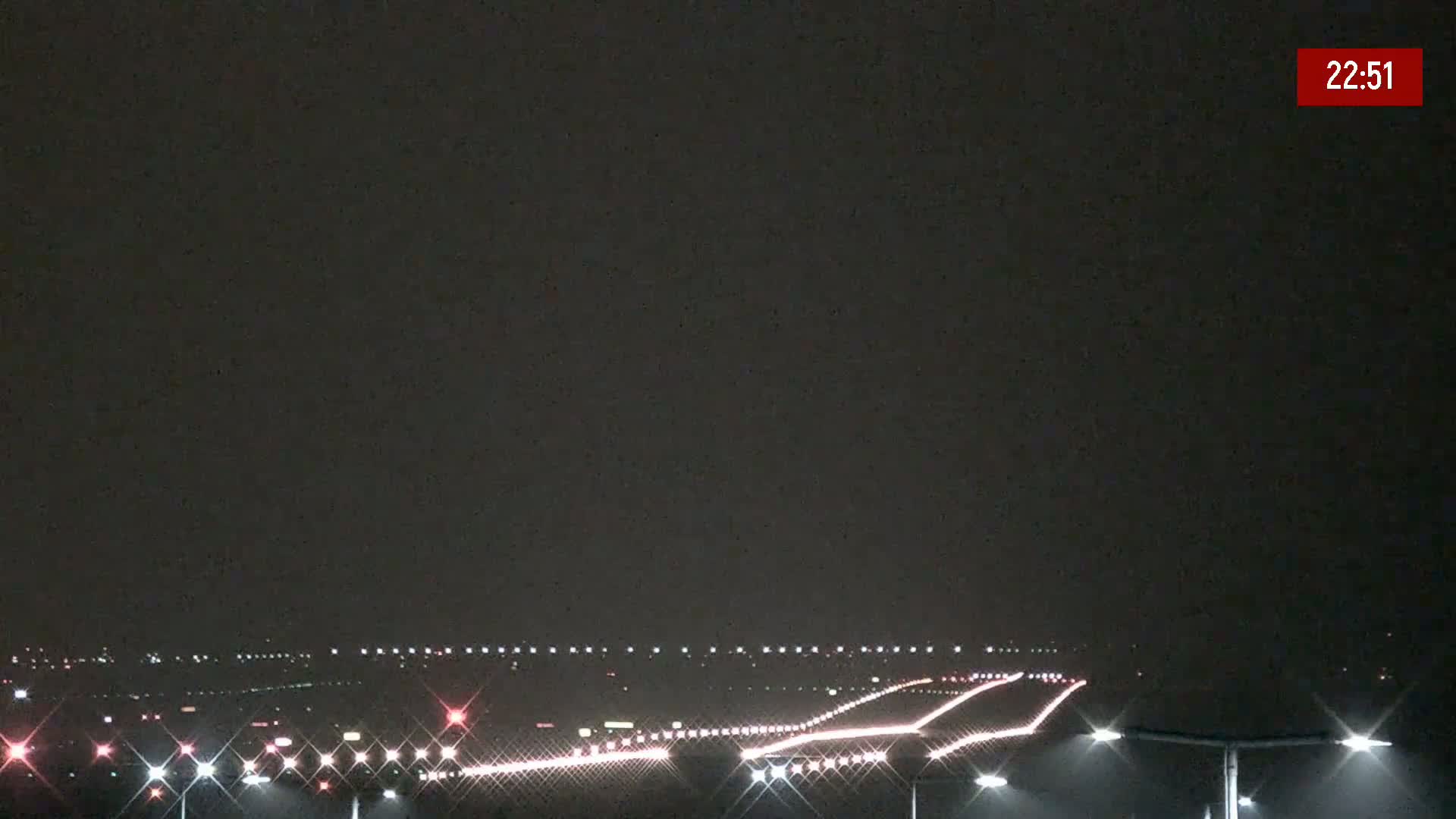 A nighttime view of an airport runway lit with lights under a dark, overcast sky.