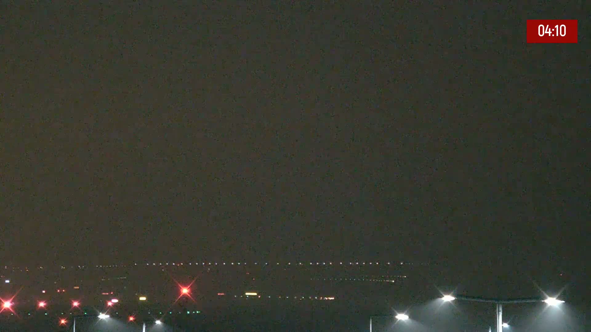 A nighttime long shot of an airport runway with lights illuminating the tarmac under a dark, overcast sky.