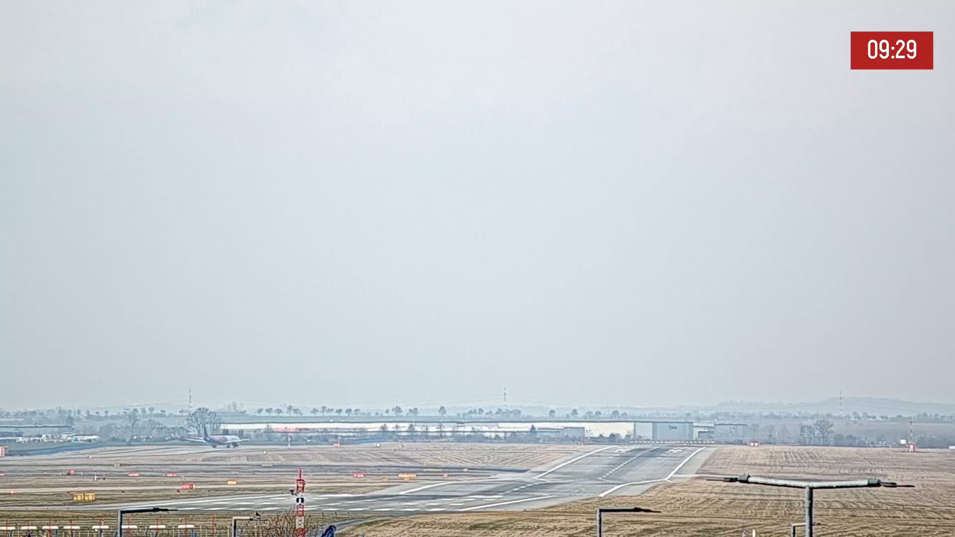 A hazy view of an airport runway with a plane on the tarmac, under a light overcast sky.